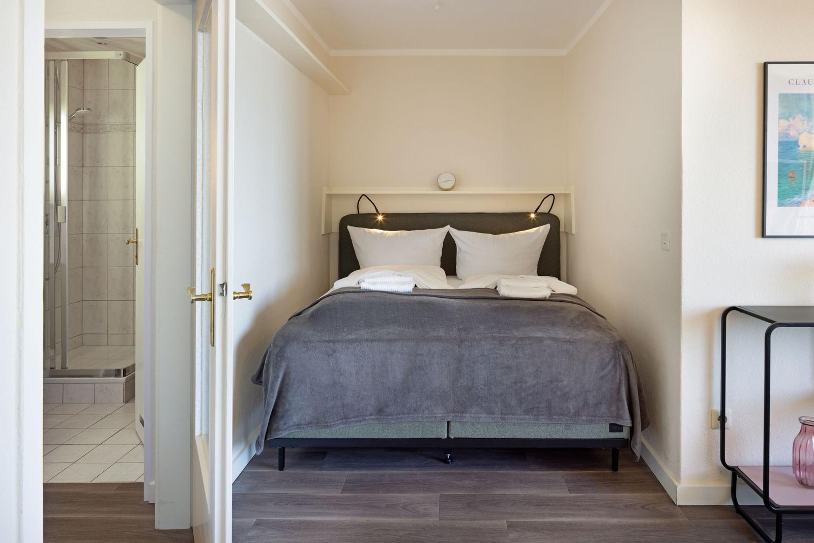 Schlafzimmer mit Bett, Wanduhr und Türe zum Badezimmer.