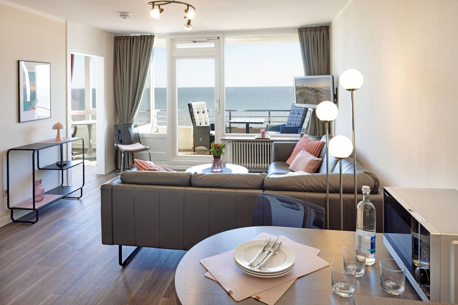 Wohnzimmer mit Sofa, Esstisch und Meerblick durch Glastür