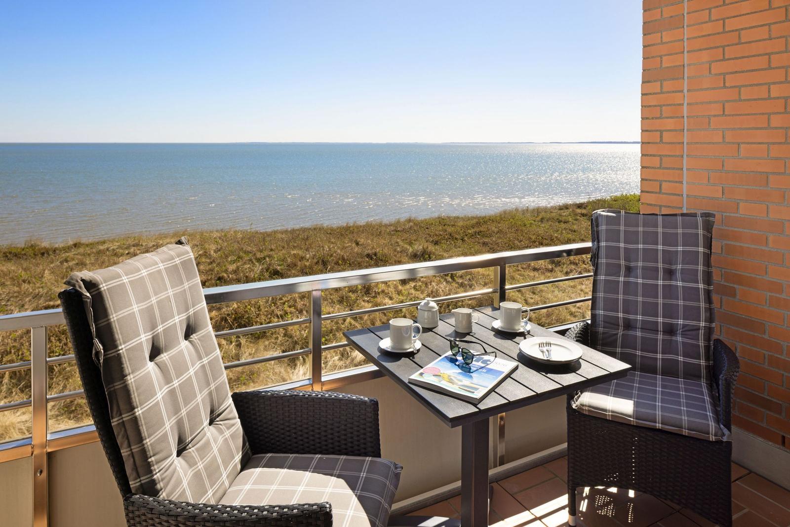 Terrasse mit Tisch und zwei Stühlen, Blick auf Meer und Grasland.