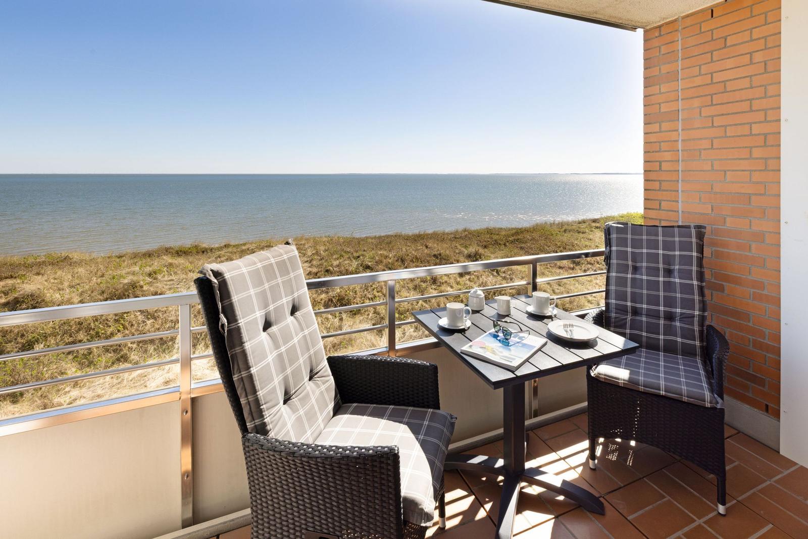 Terrasse mit Tisch und zwei Stühlen bietet Meerblick. Hintergrund: Strand und Meer.