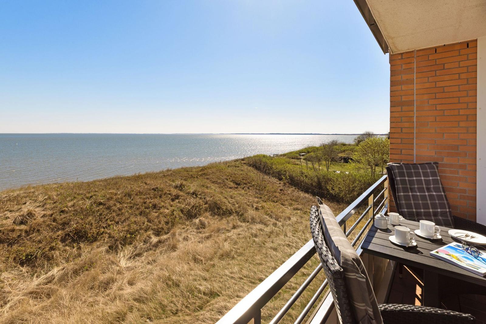 Terrasse mit Tisch und Stühlen bietet Blick auf Wasser und Grasland.
