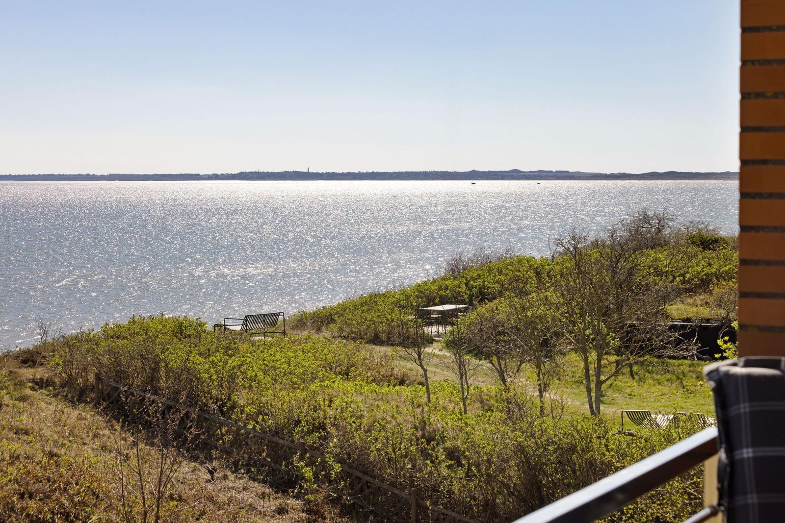 Blick auf ruhiges Wasser mit grüner Vegetation und Sitzgelegenheiten im Vordergrund.