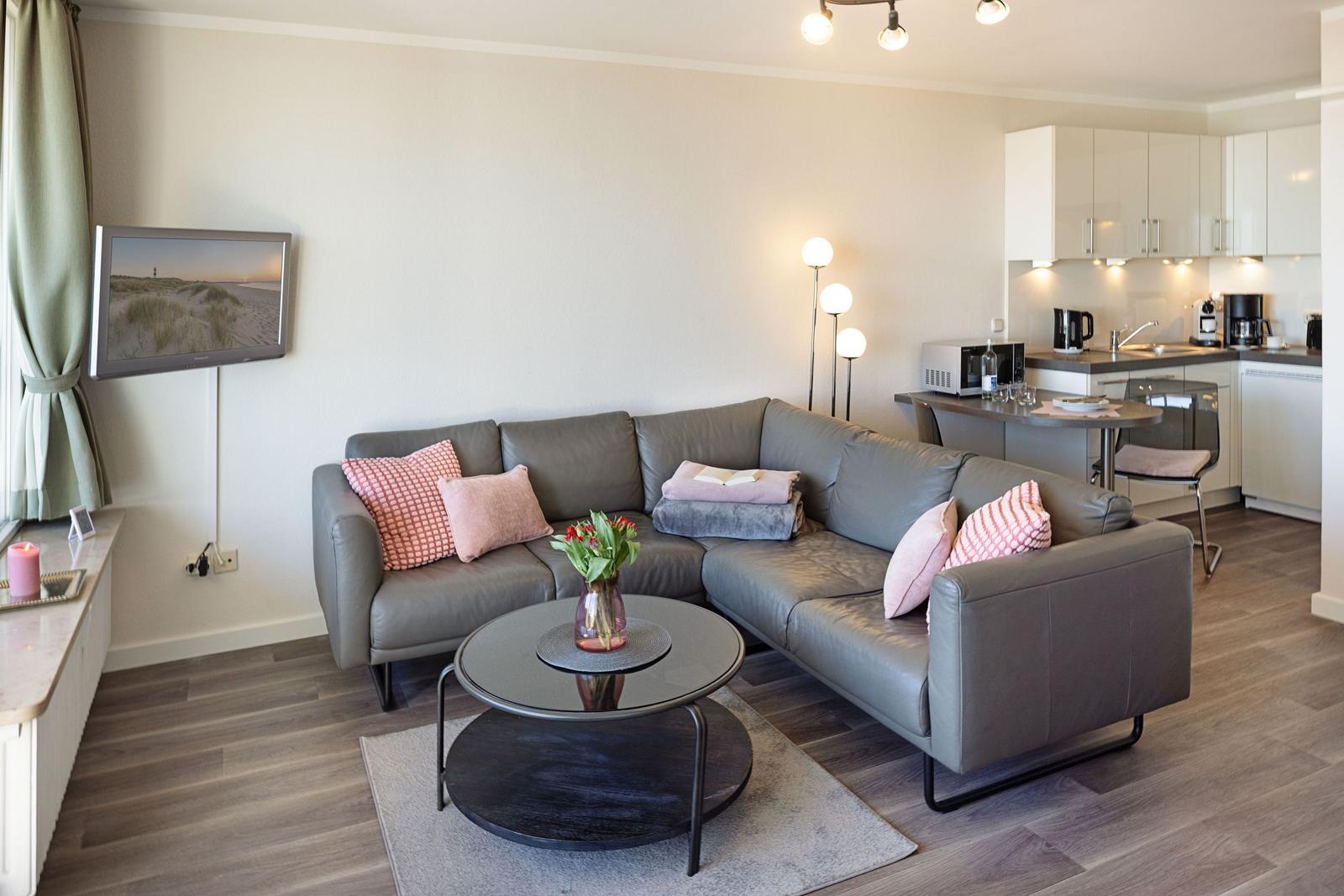 Ein Wohnzimmer mit grauem Sofa, runden Tisch und Küchenbereich im Hintergrund.