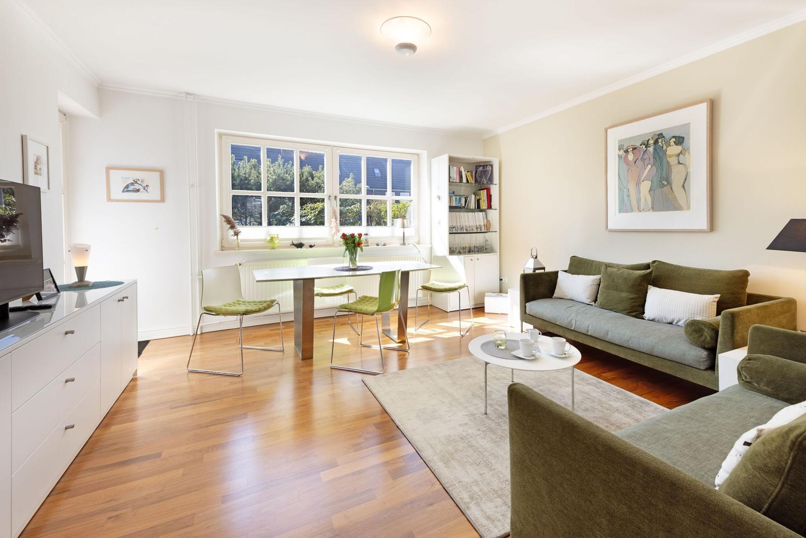 Living room with dining table, sofa, and bookcase. Wooden floor and window with view.