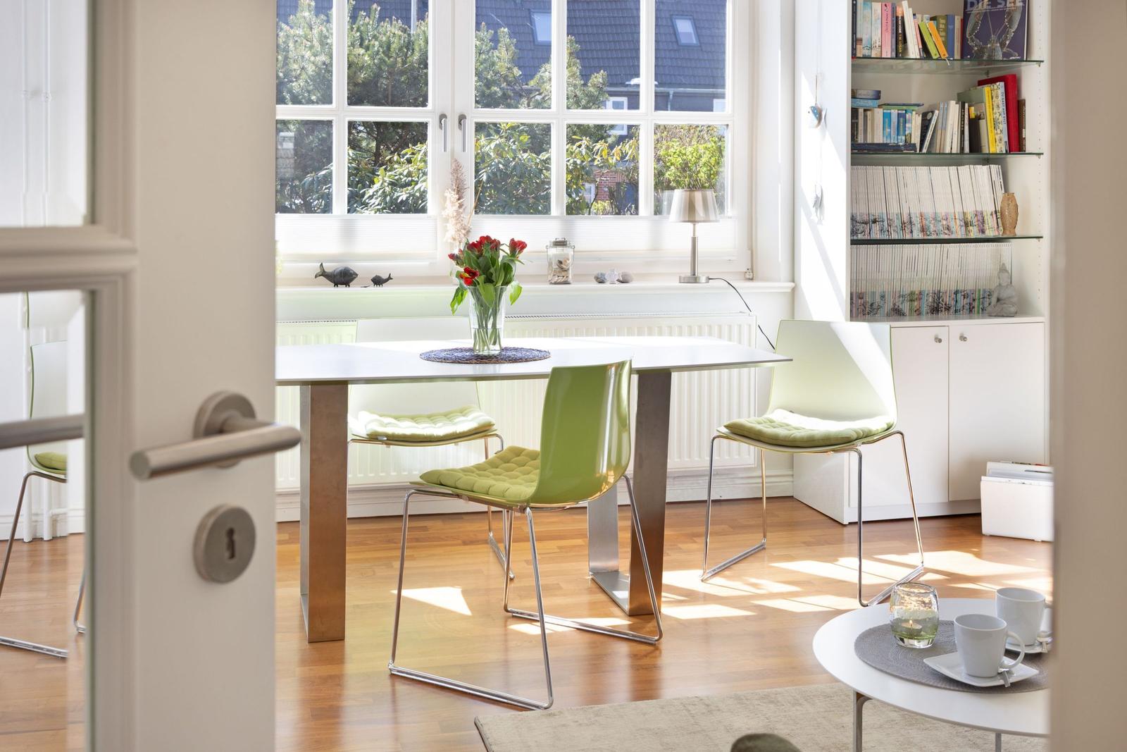 Dining room with green chairs, table, and bookshelf. Window with view of garden.