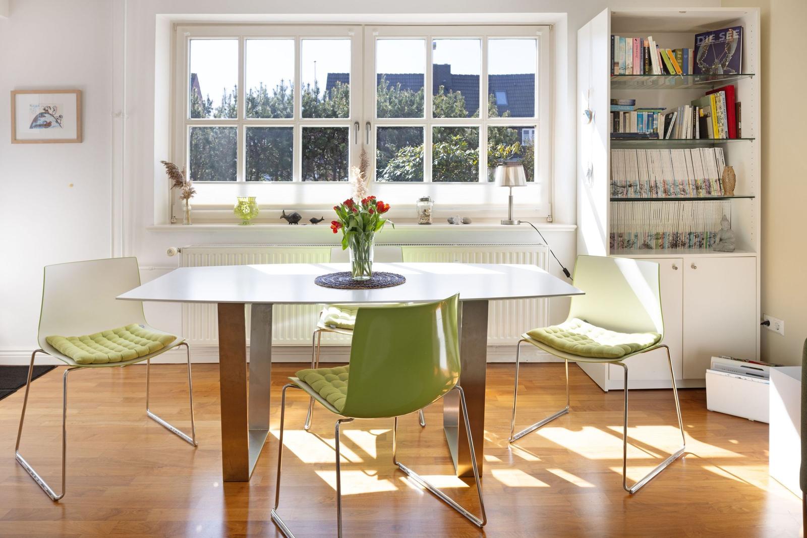 Dining table with green chairs in front of large window with tree view.