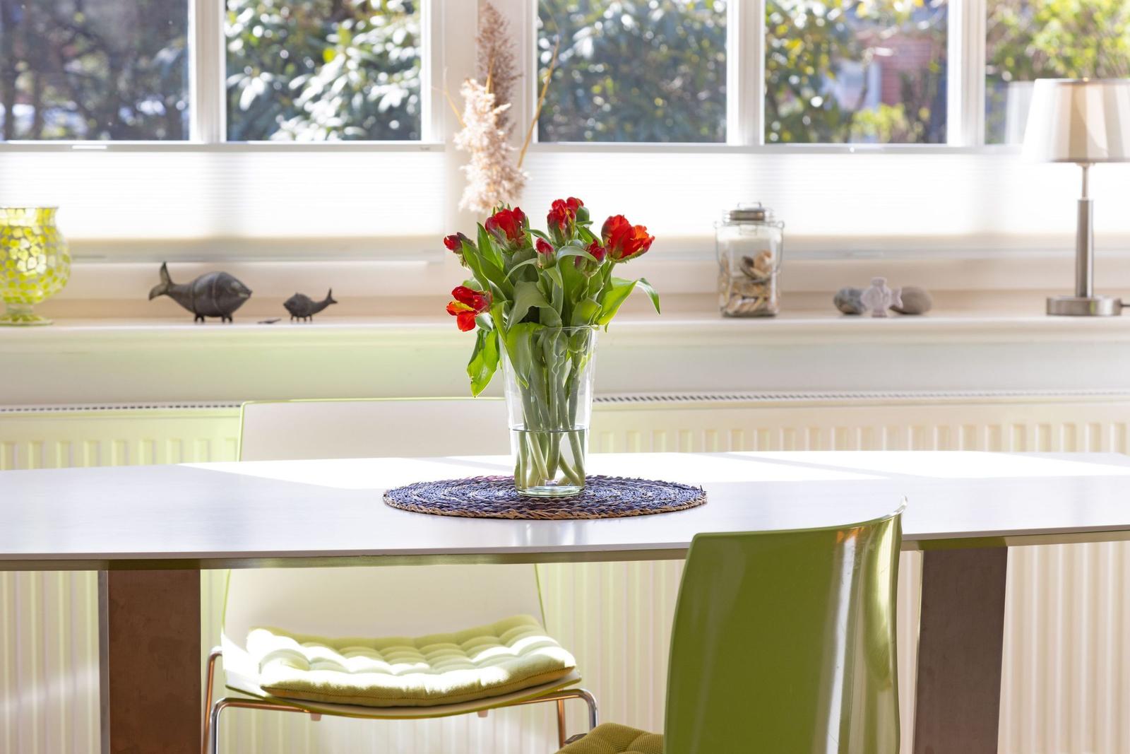 Table with flowers, green chairs, and window with garden view.