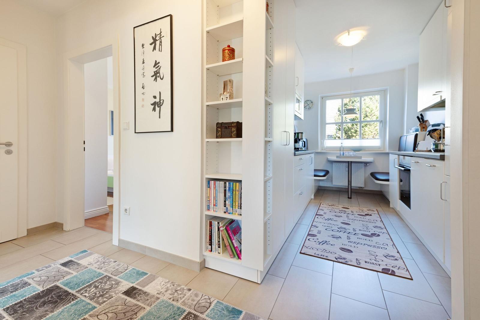 Kitchen with window, bookshelf, and coffee-themed rug.