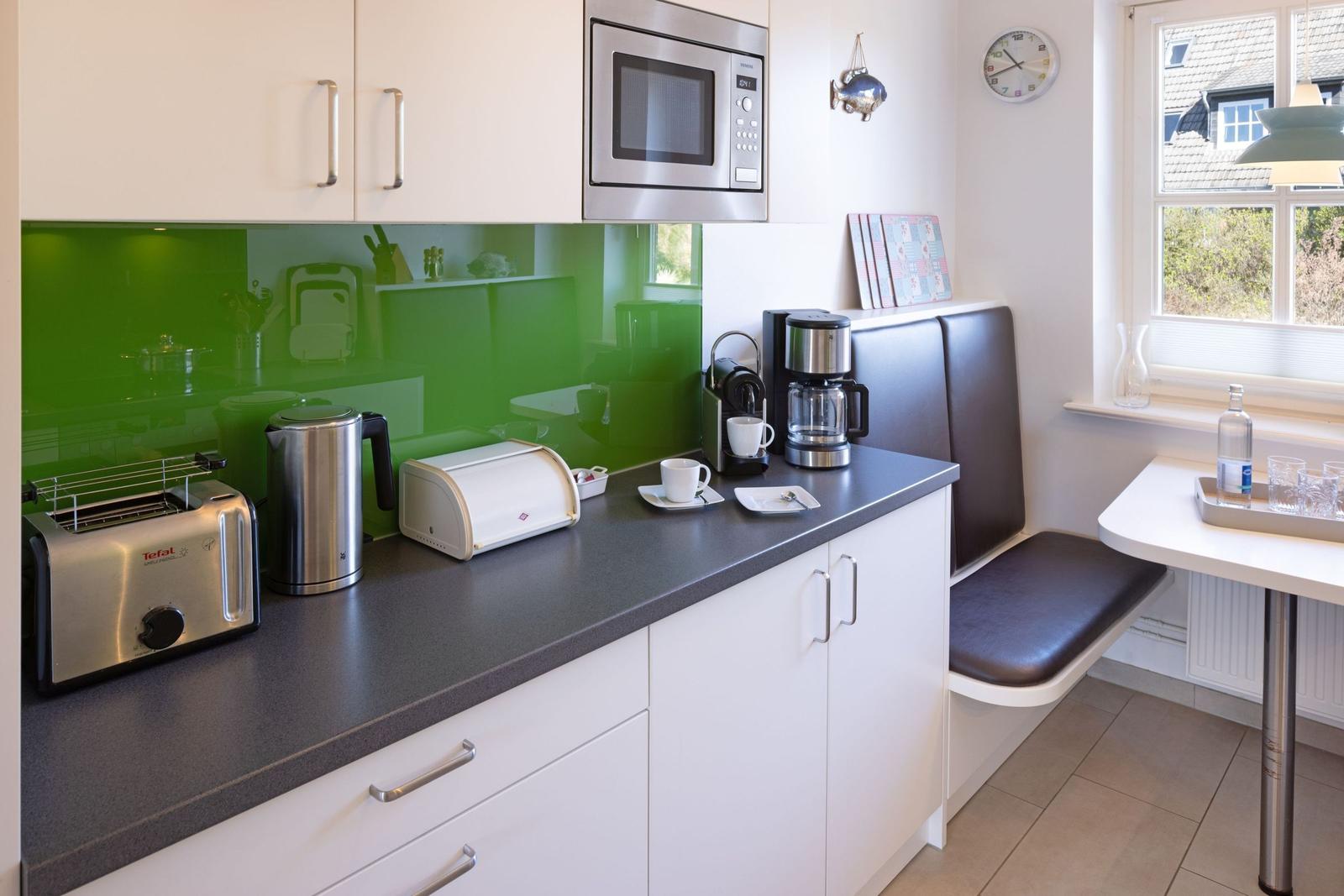Kitchen with worktop, microwave, coffee machine, and bench by the window.
