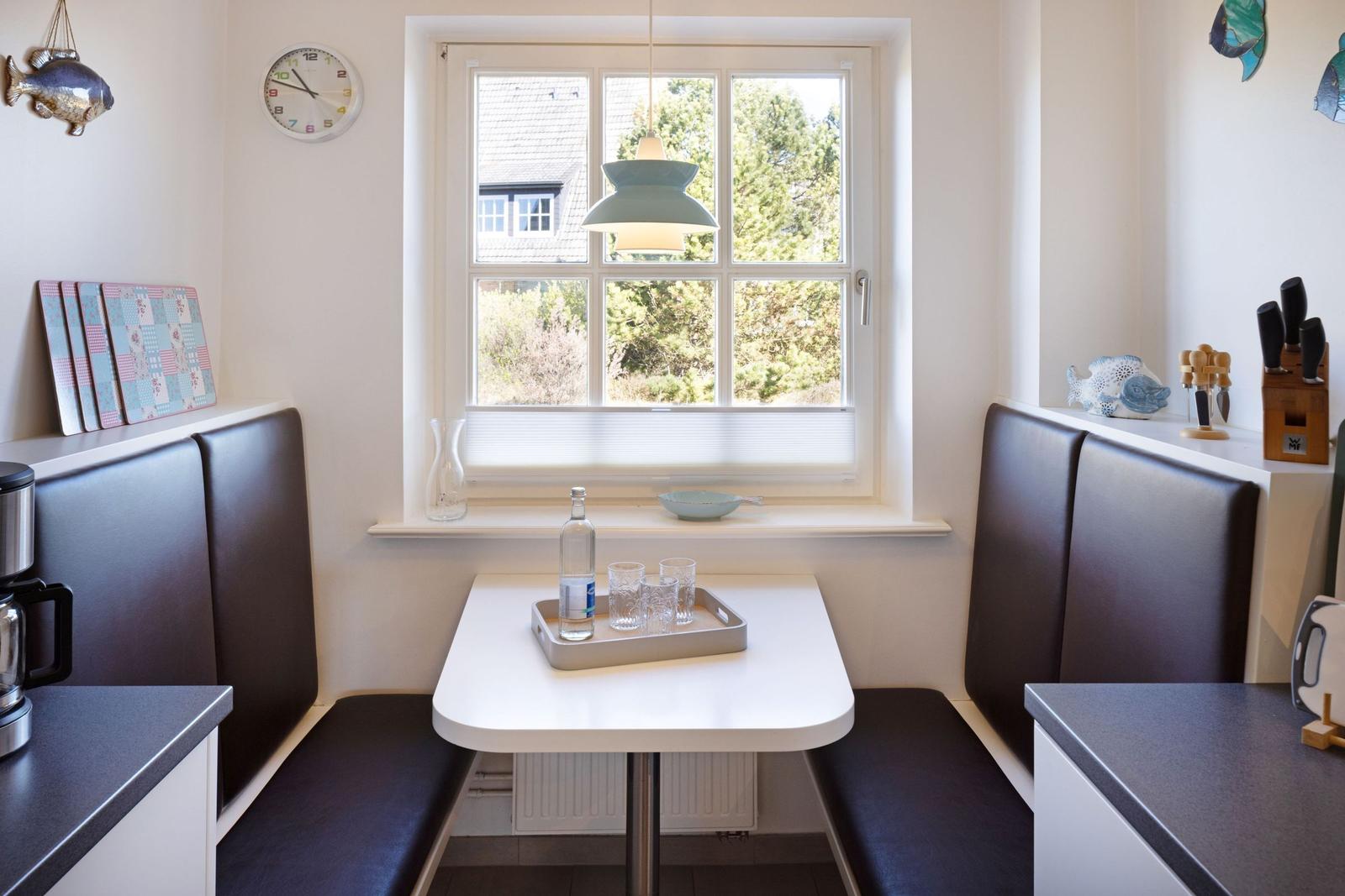 Dining area with table and seating by window overlooking greenery.