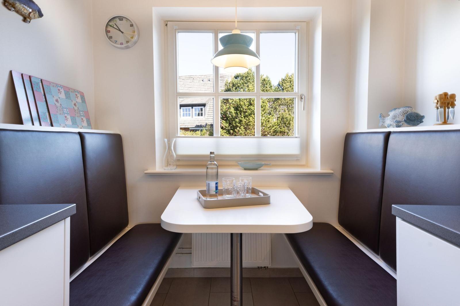 Dining area with table and bench under window. On table: tray with glasses and water bottle.