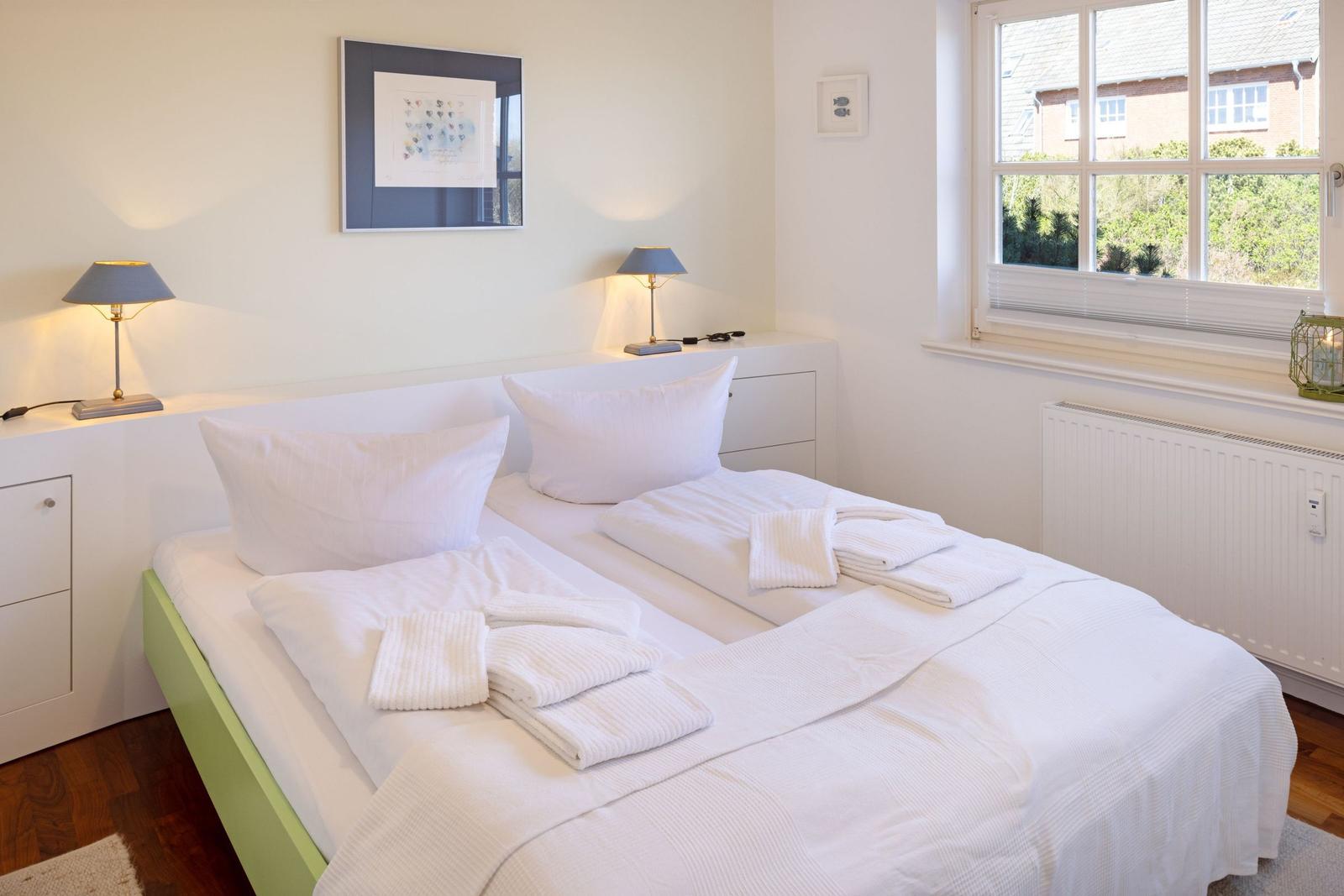 Bedroom with double bed, white linens, and window view of greenery.