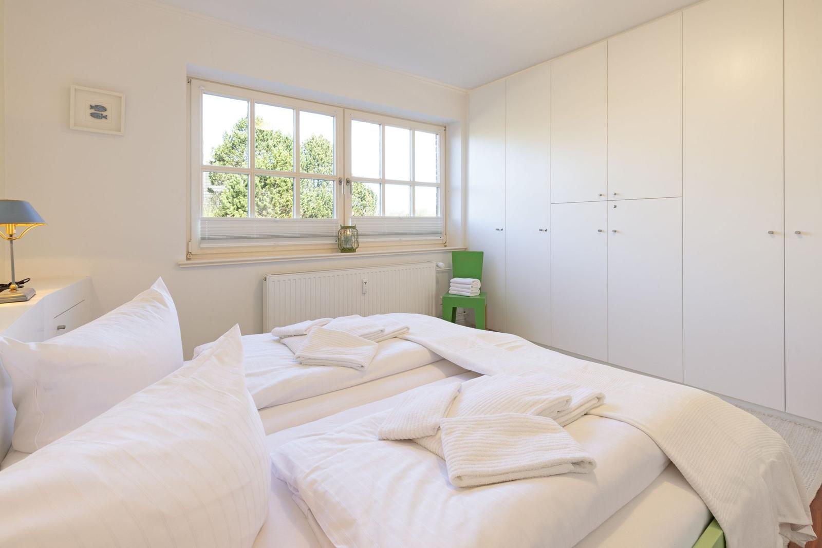 Bedroom with double bed, window, and white wardrobes.