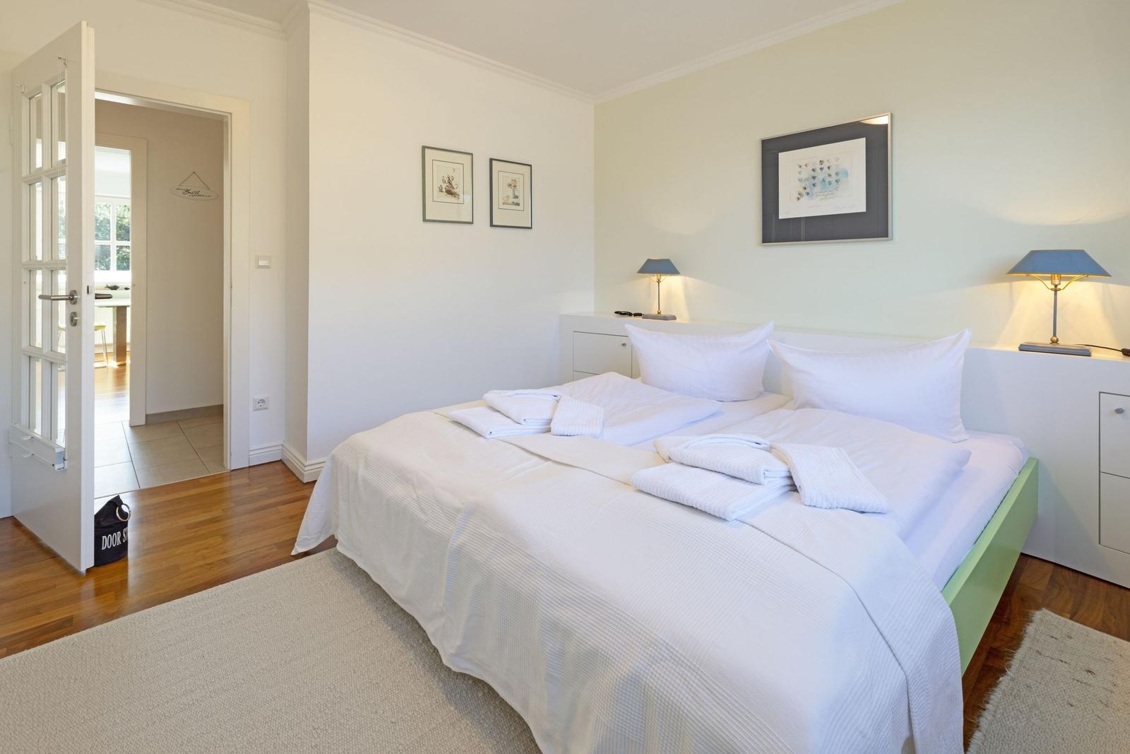 Bedroom with bed, nightstands, and pictures on the wall. Door leads to the kitchen.