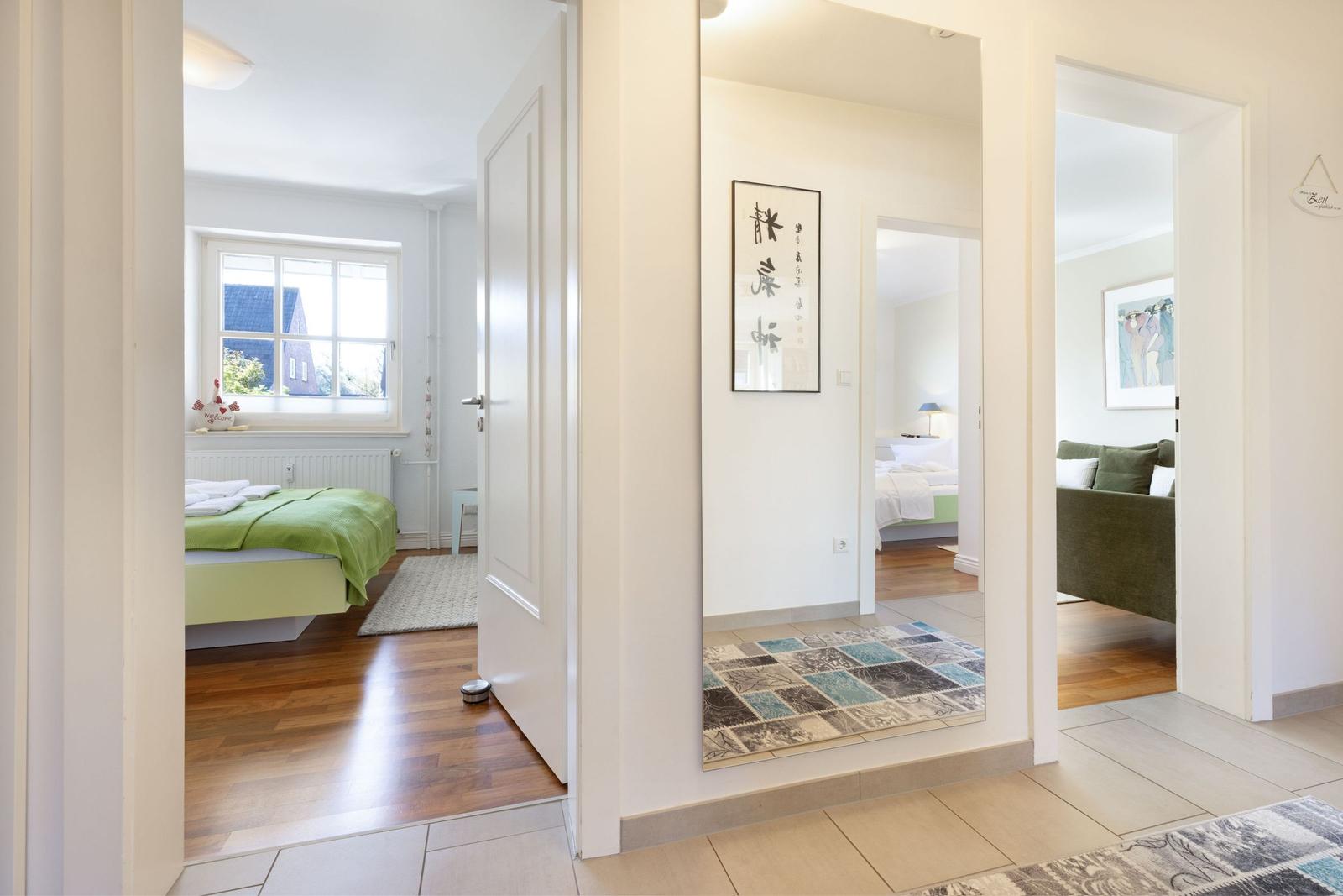 Hallway with view into bedrooms and living area. Wooden floors and rugs visible.