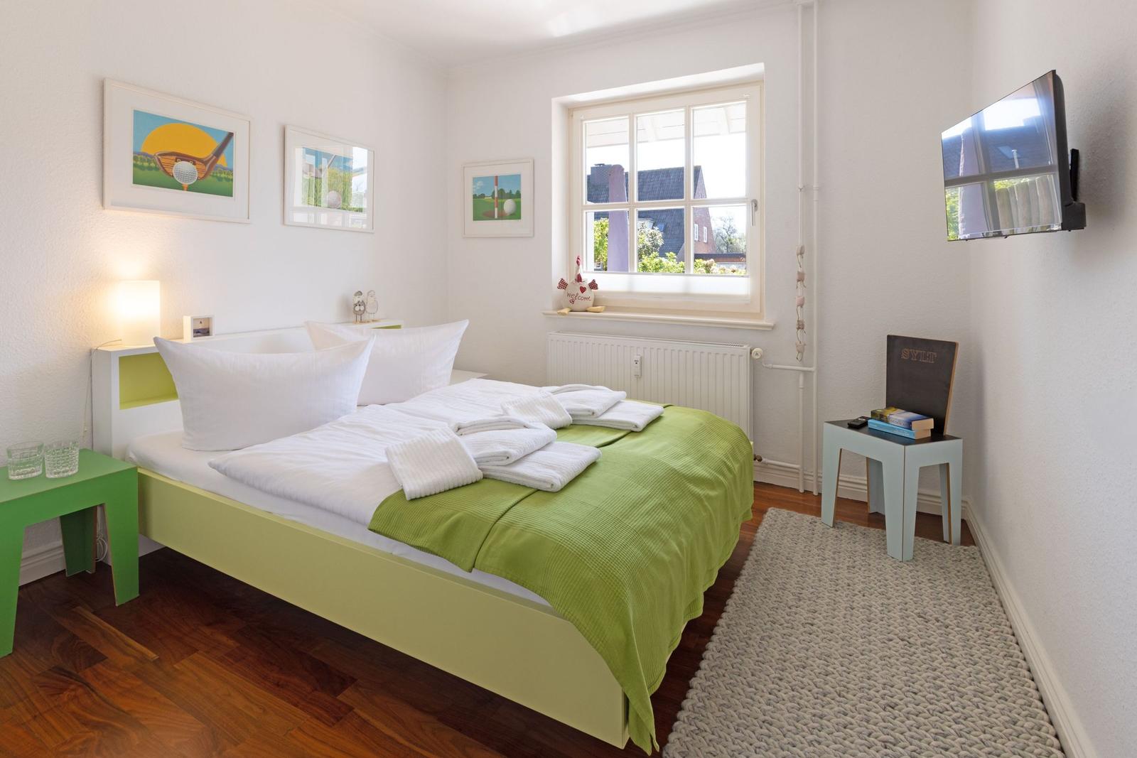 Bedroom with bed, window, TV, and decorative pictures on the wall.