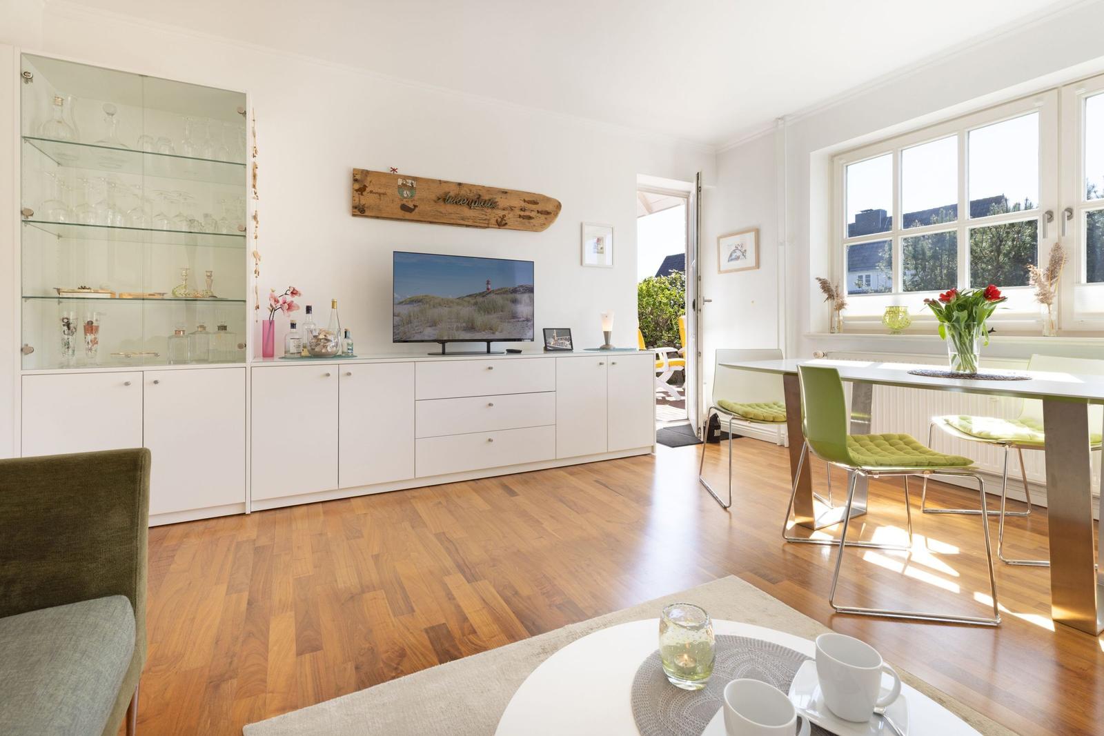 Living and dining area with wooden floor, TV, dining table, and windows.
