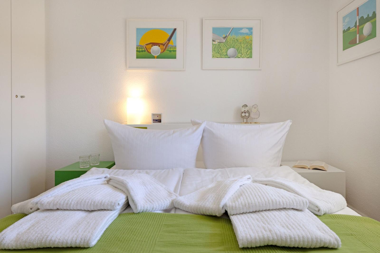 Bedroom with bed, white pillows, and green bedspread. Golf-themed pictures hang on the wall.