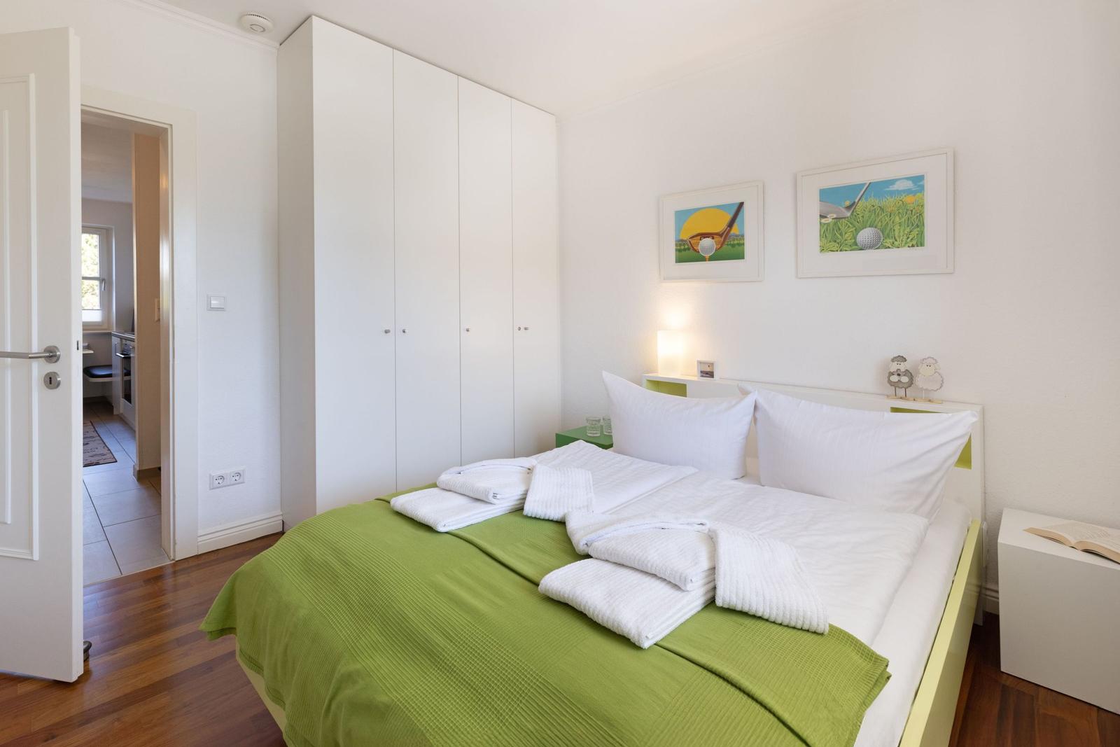 Bedroom with bed, wardrobe, and wall art. View into kitchen through doorway.