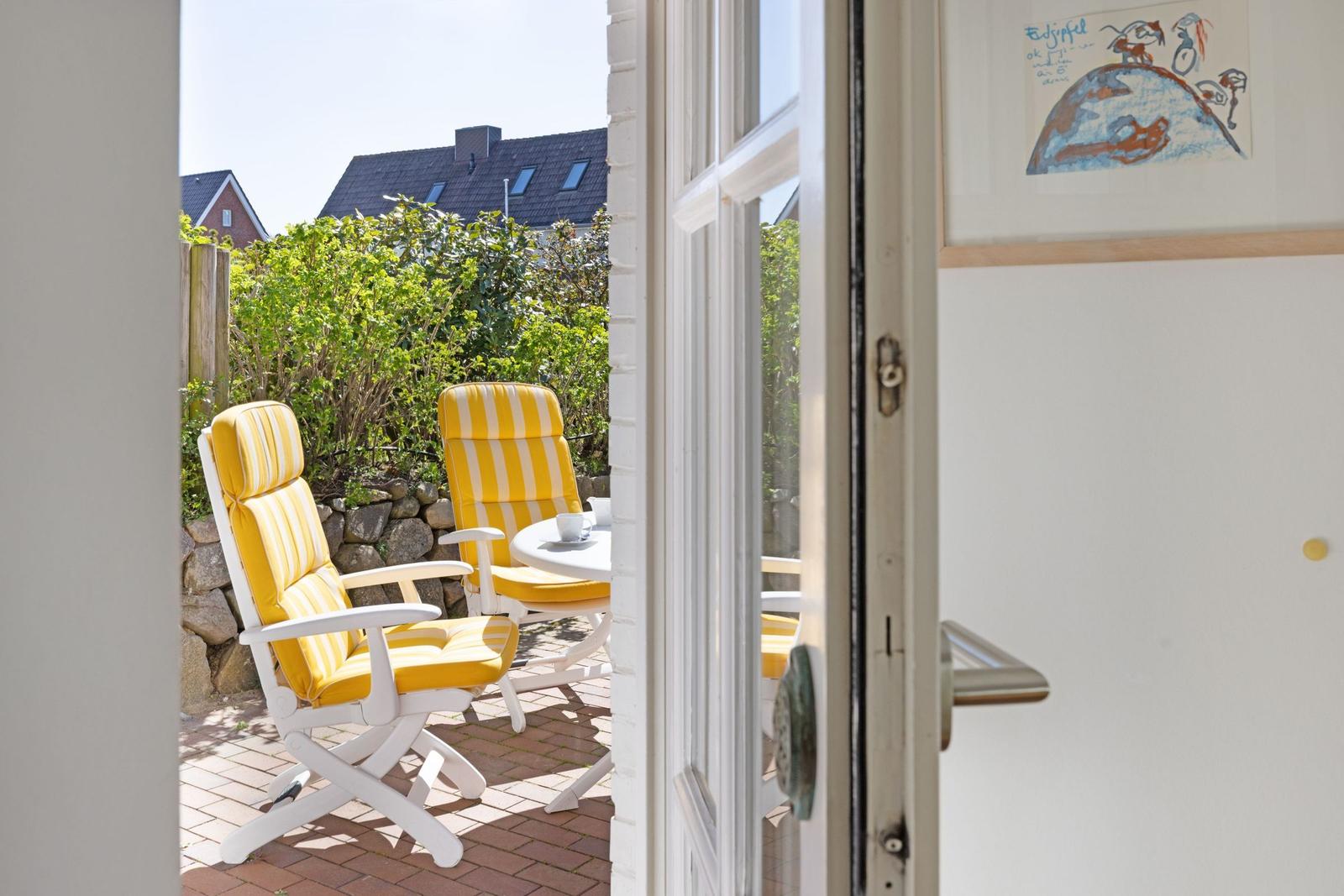 Through the door, a terrace with two yellow chairs and a table is visible.