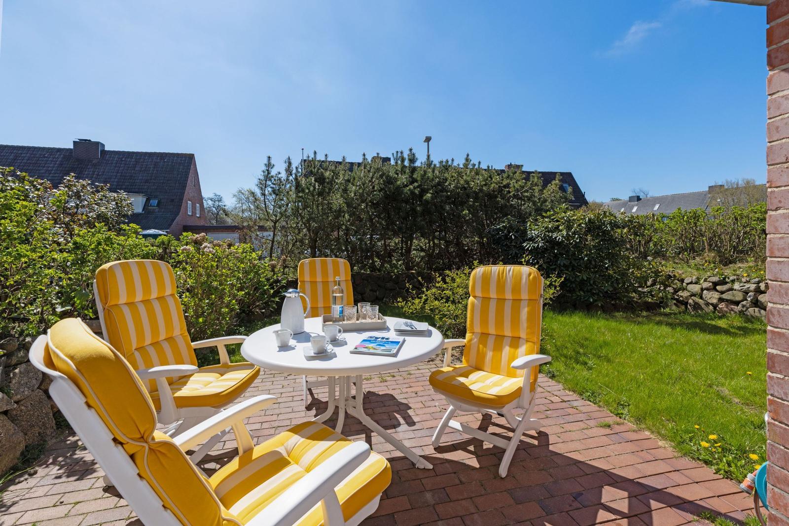 Terrace with four yellow chairs and round table. Green areas and houses in the background.