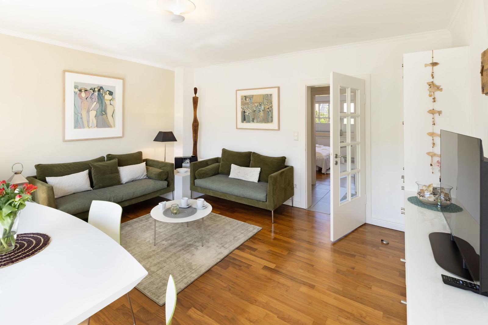 Living room with two green sofas, wooden floor, and TV on the wall.