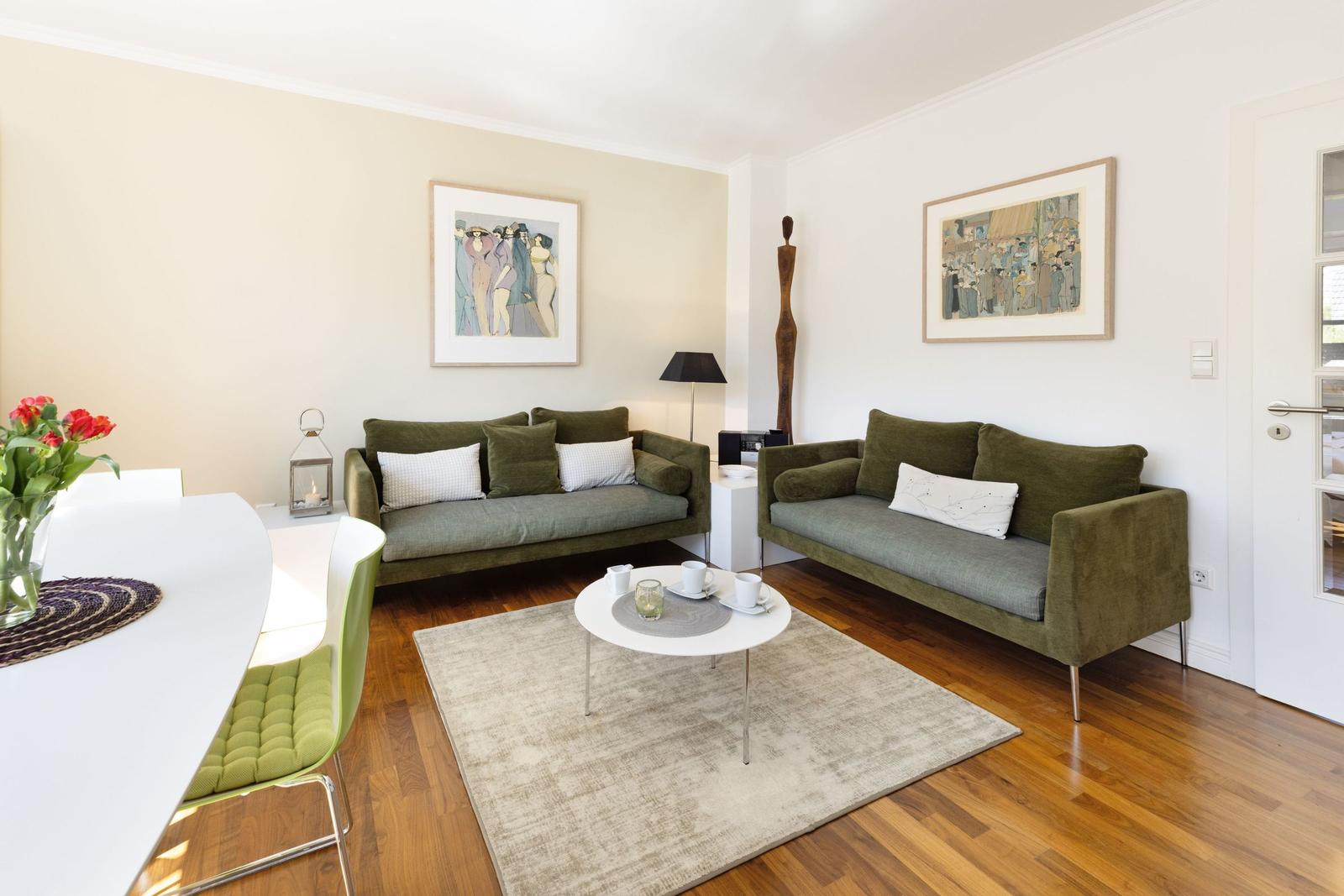 Two green sofas, a round table, pictures on the walls, and hardwood floor.