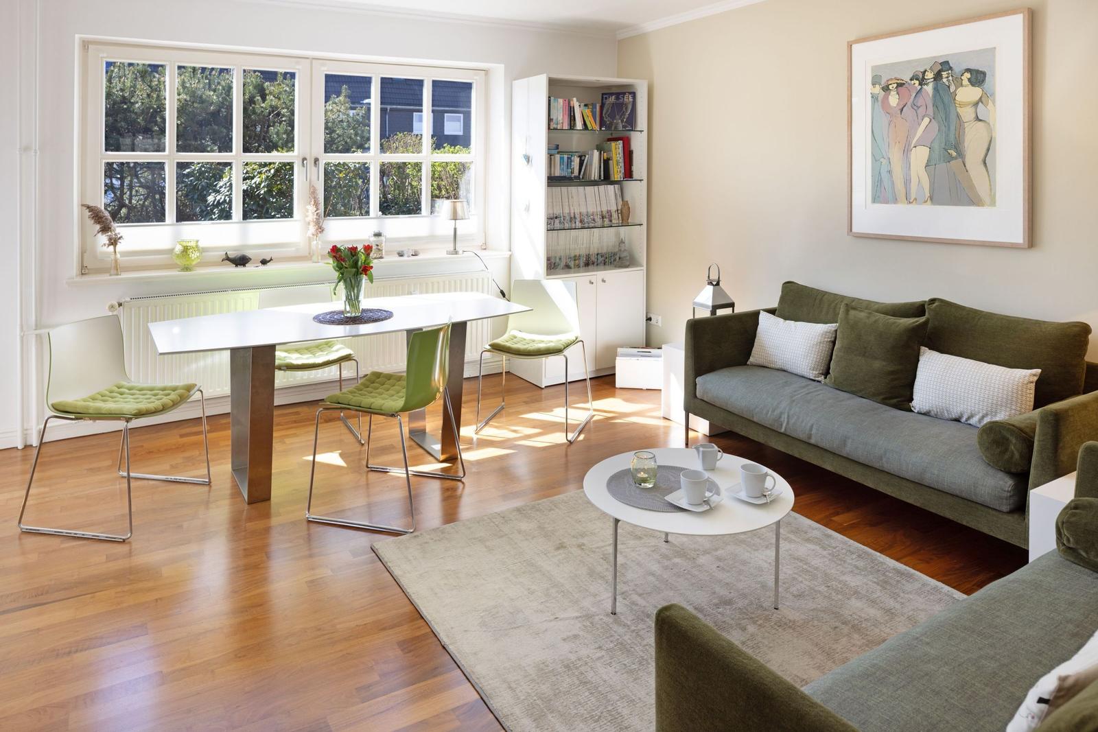Living and dining area with sofa, table and chairs. Large windows, bookcase and wall art.