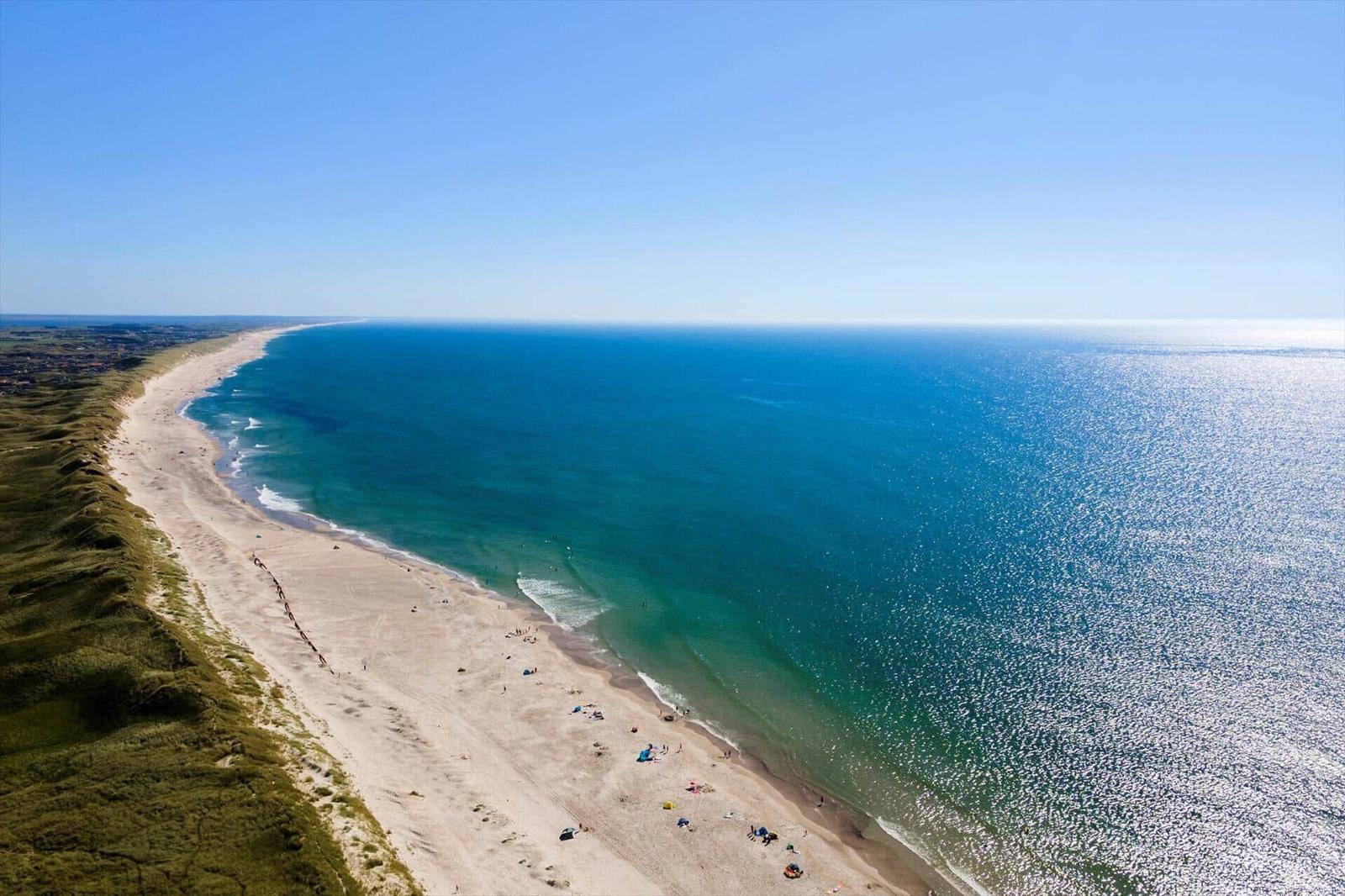 View of a long beach with turquoise sea and green dunes.