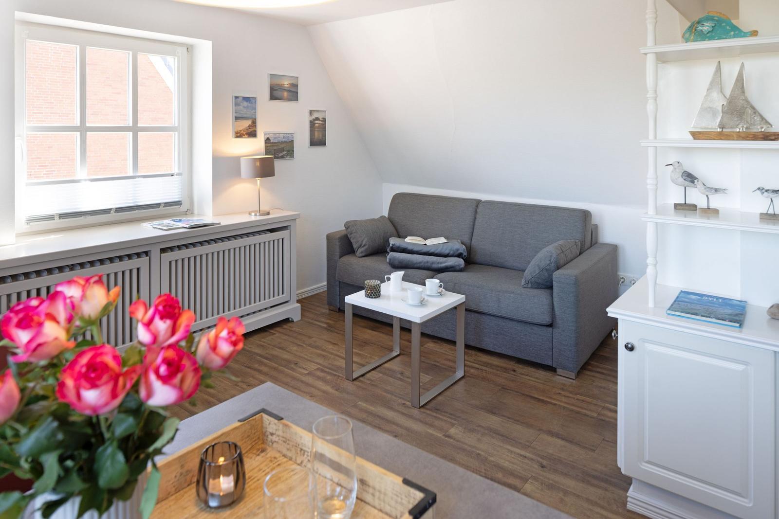 Wohnzimmer mit grauem Sofa, Holzboden und Fenster mit Blick auf Backsteinhaus.