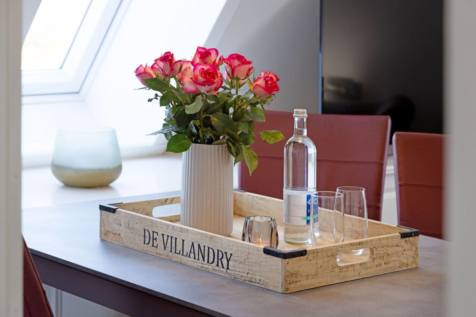 Ein Holztablett mit Rosen, Wasser und Gläsern auf einem Tisch.
