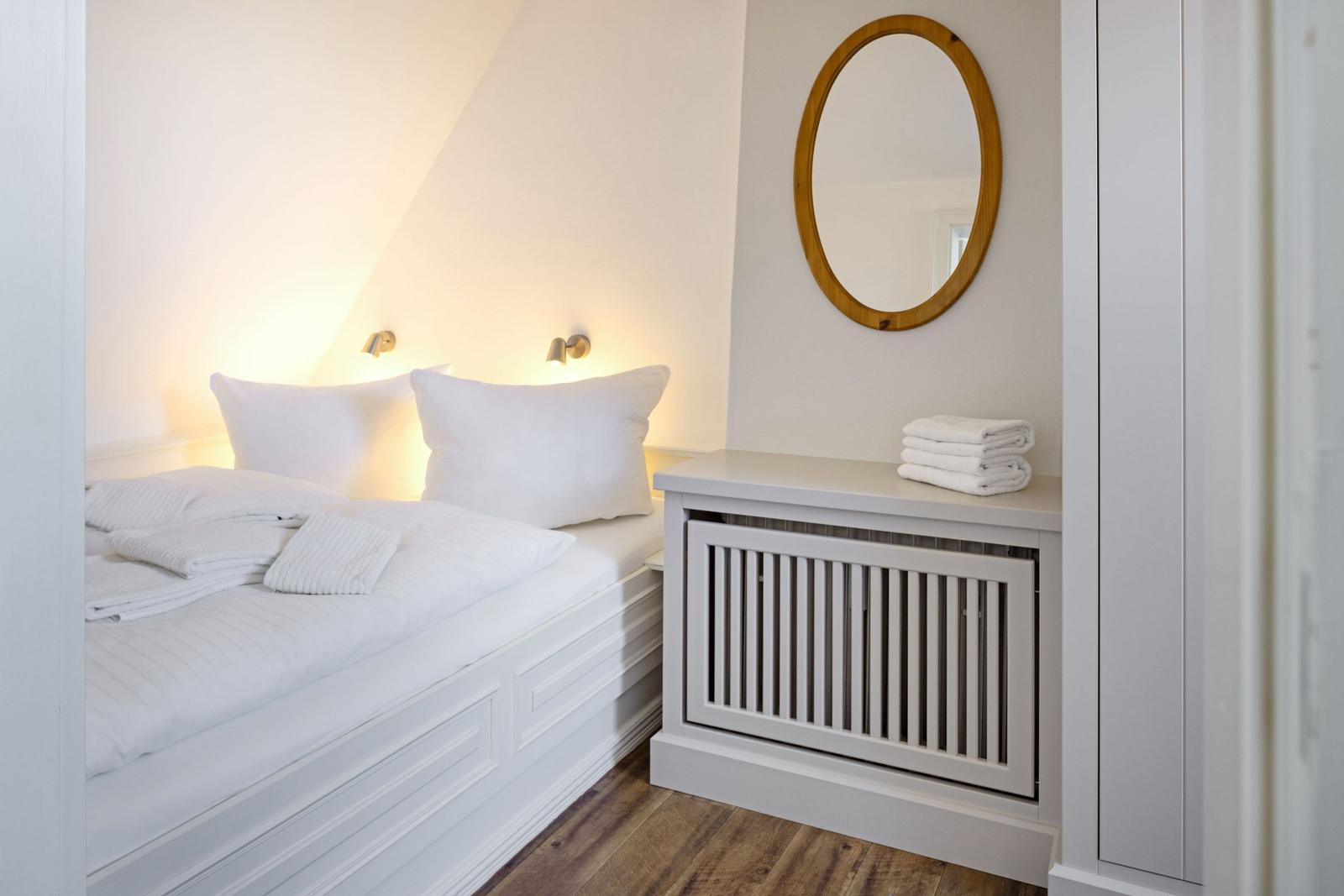 Schlafzimmer mit weißem Bett, runden Spiegel und Handtüchern.