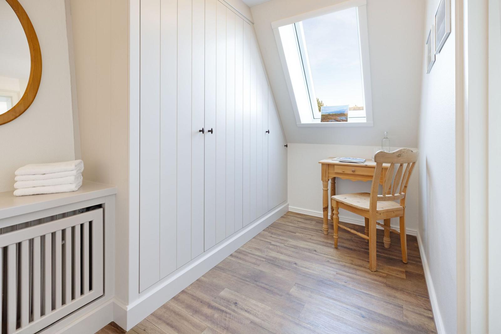 Kleines Zimmer mit Schrank, Schreibtisch und Stuhl unter Dachschrägen.