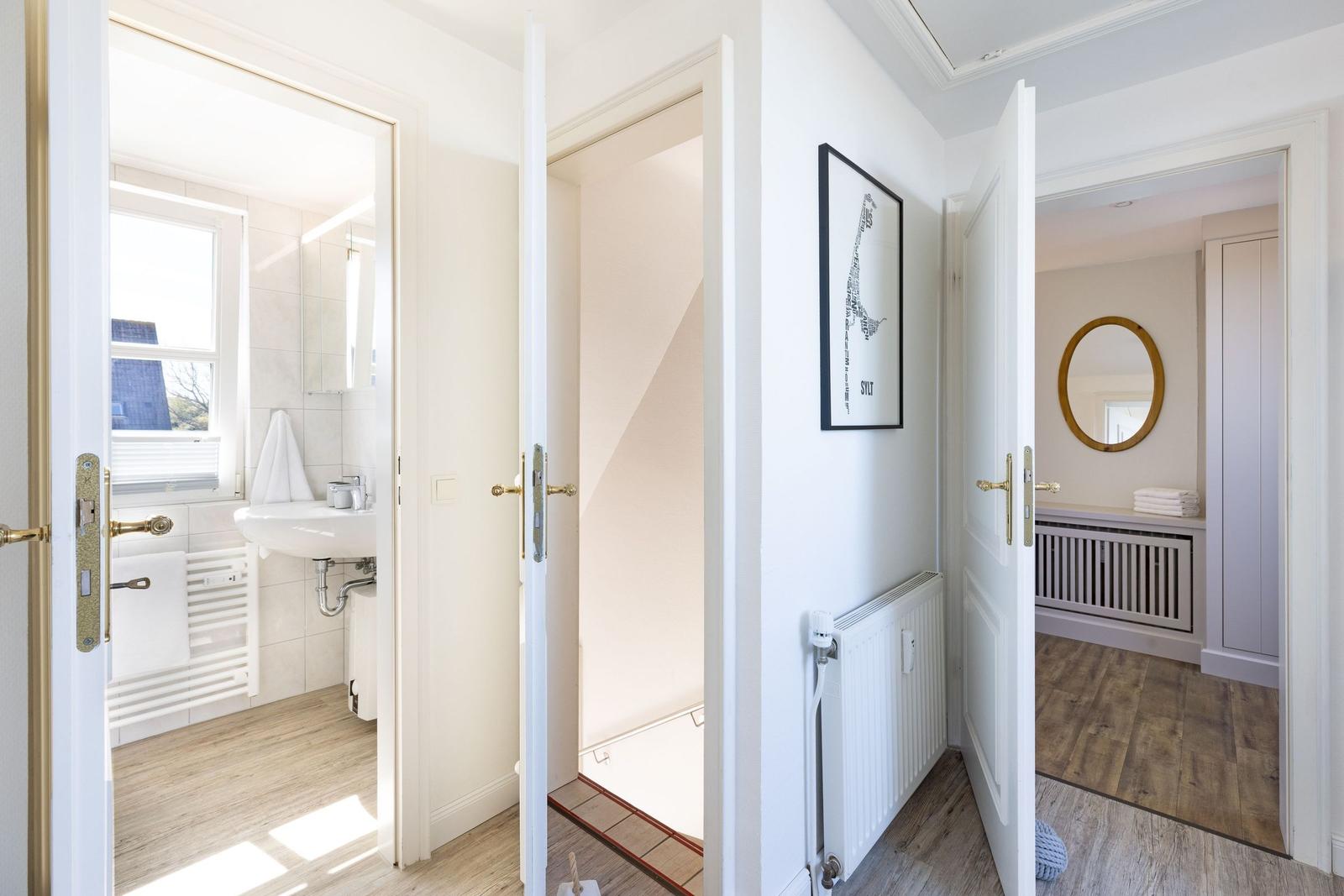 Durchgang mit Blick in Bad und Schlafzimmer. Weiße Türen, Holzboden und Wandbild.
