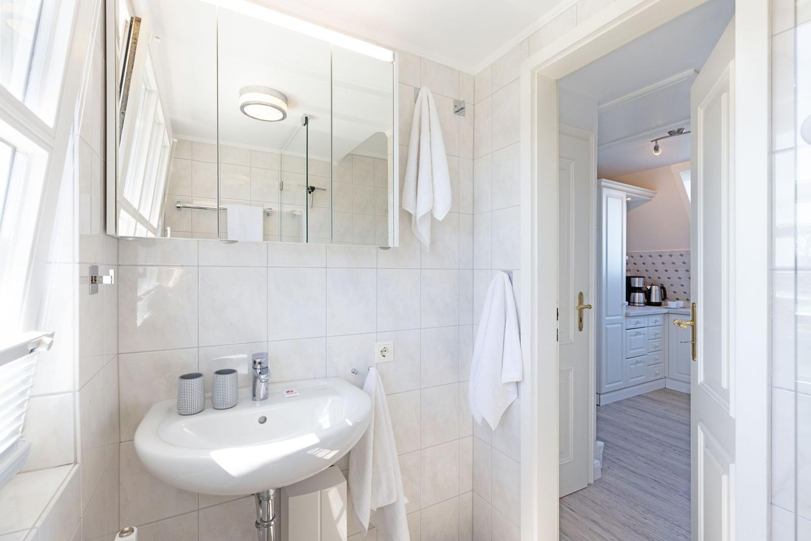 Badezimmer mit Waschbecken, Spiegel und Dusche. Tür führt in die Küche.