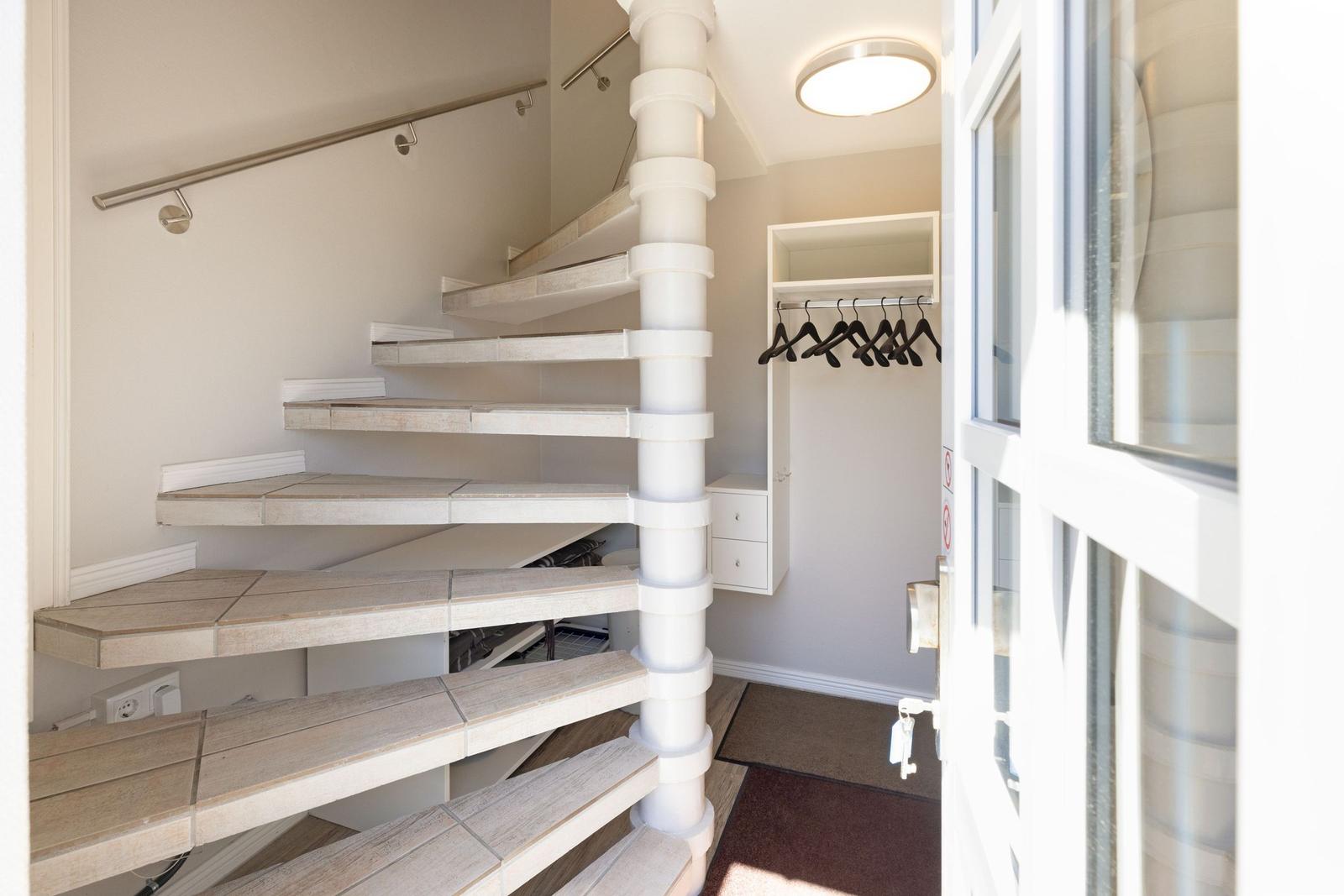 Spiralförmige Treppe mit Holzstufen und weißem Mittelpfosten. Neben dem Treppenhaus befindet sich ein Kleiderschrank.