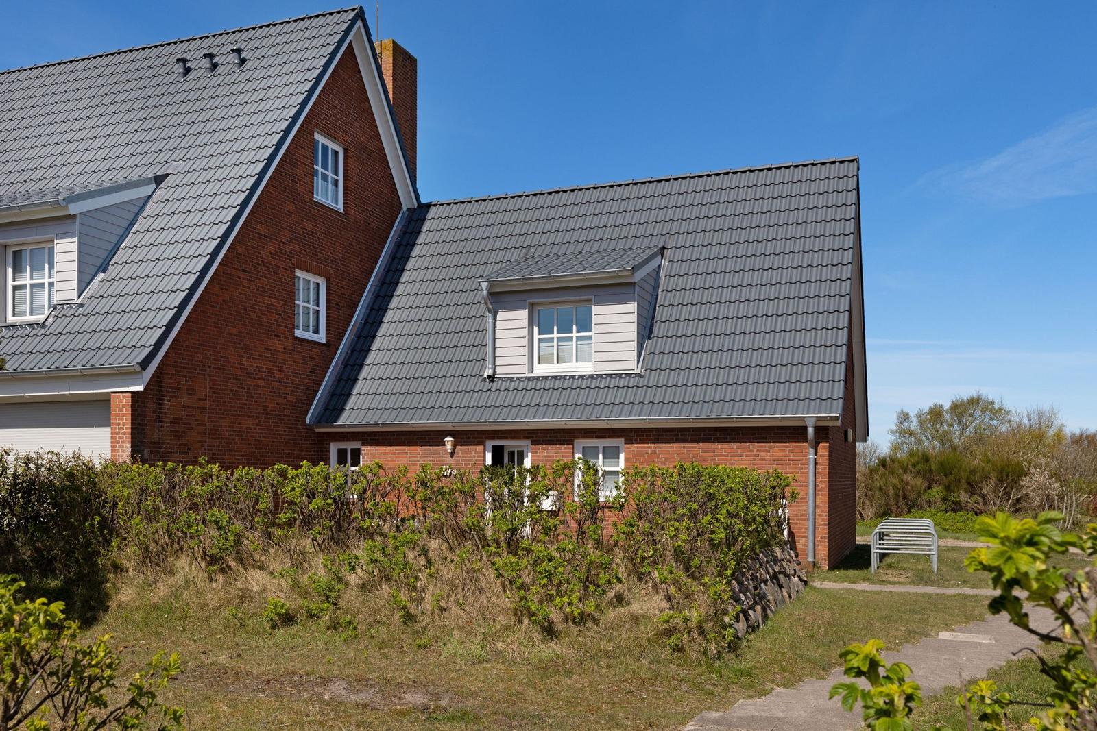 Rotes Backsteinhaus mit grauem Dach und grüner Umgebung unter blauem Himmel.