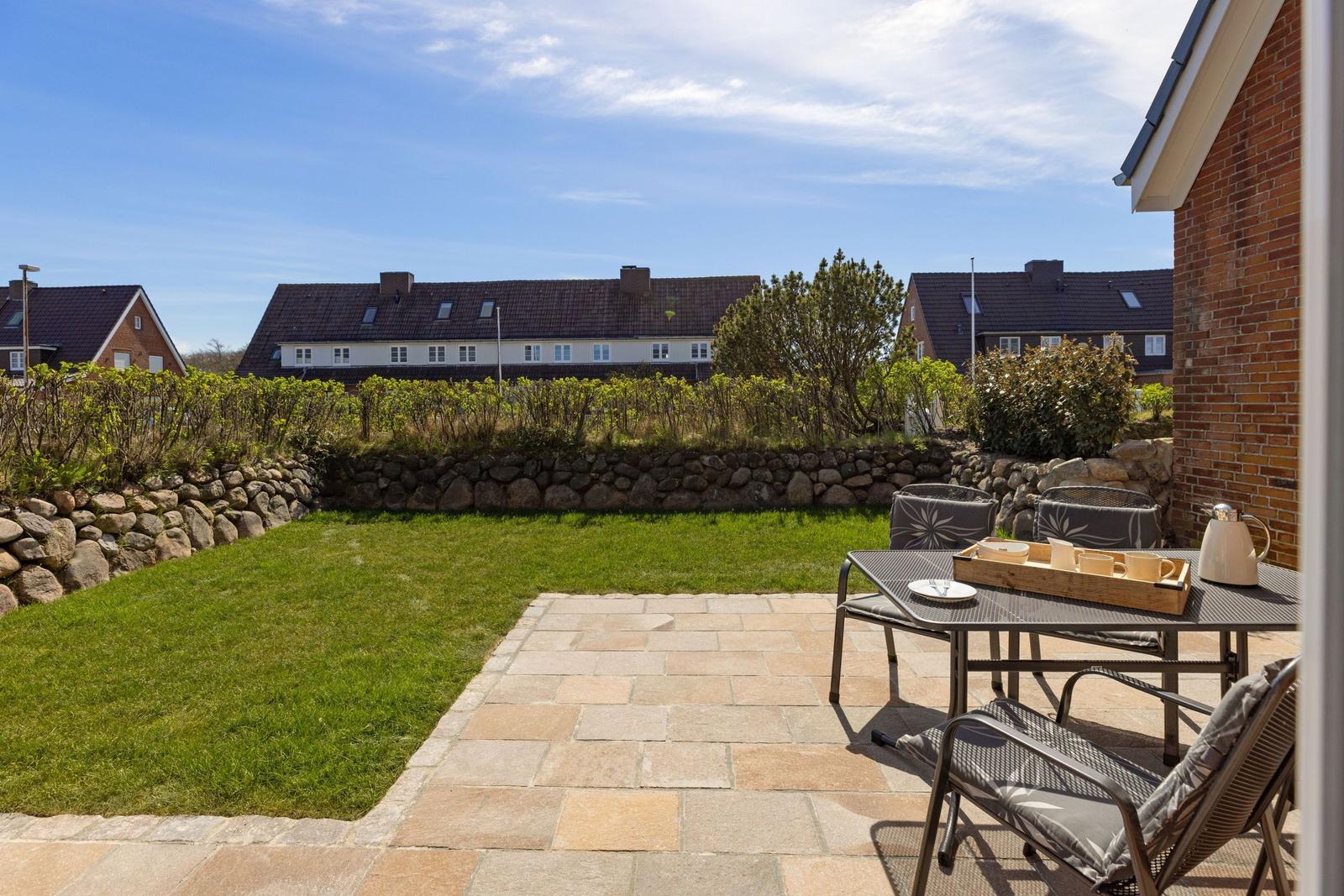 Terrasse mit Tisch und Stühlen, Grasfläche und Steinmauer im Hintergrund.