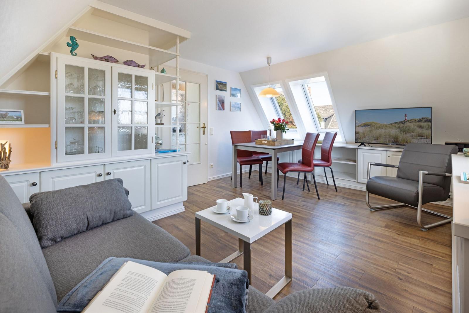 Wohn- und Essbereich mit Sofa, Tisch, Stühlen und TV. Dachfenster und Holzboden.