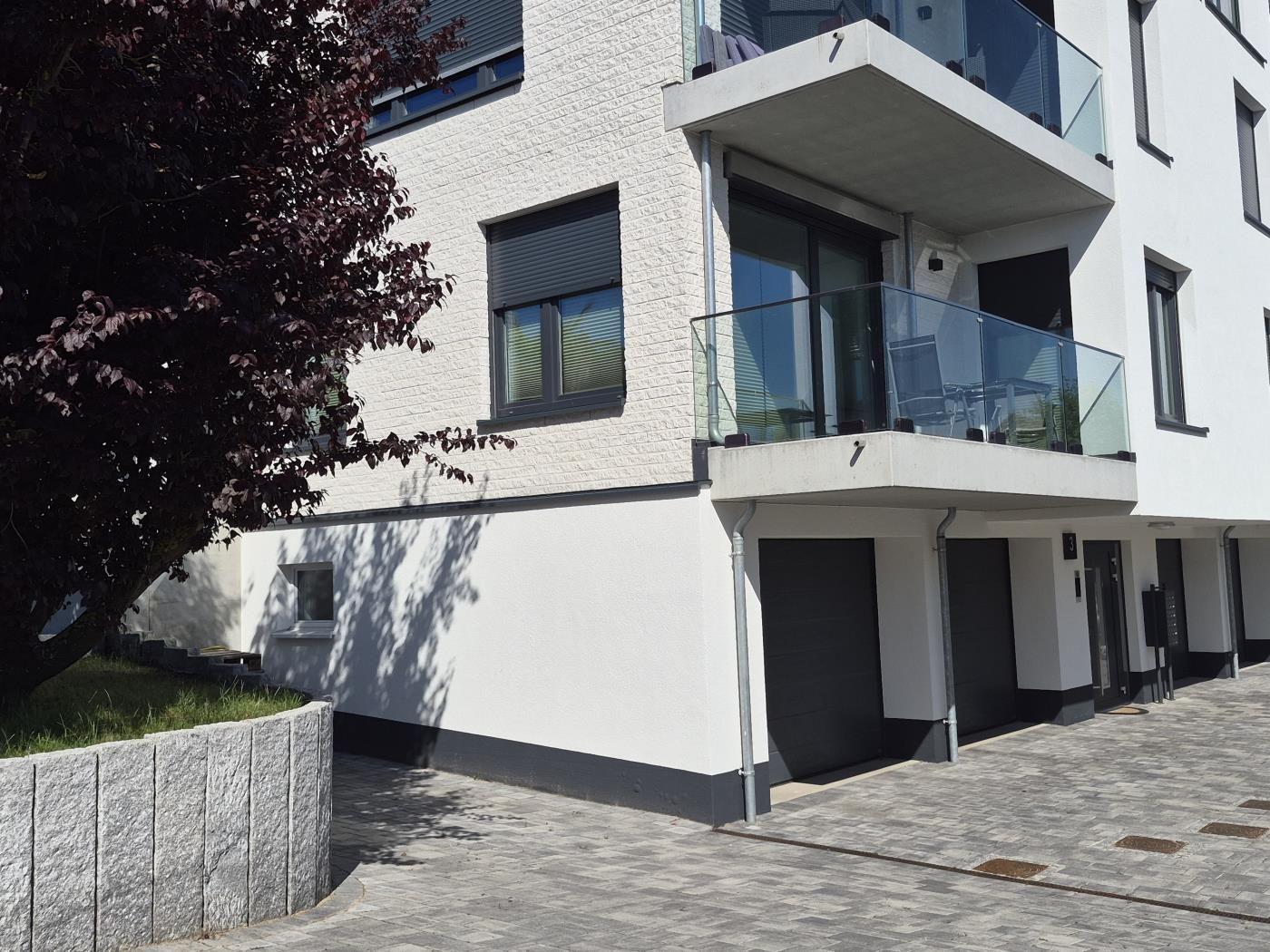 Moderne Wohnung mit Balkon und Garage. Außenbereich mit Baum und Steinmauer.