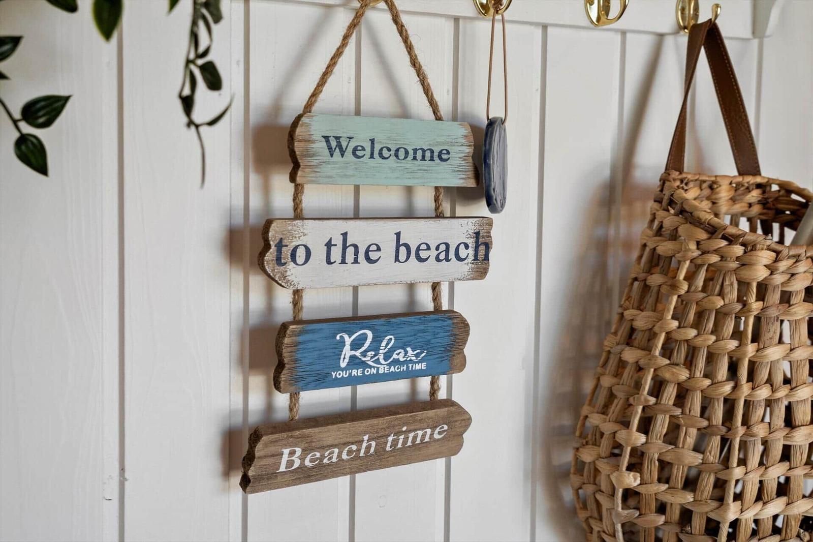 Willkommen an der Küste. Strandtasche und Schild hängen an weißer Wand.