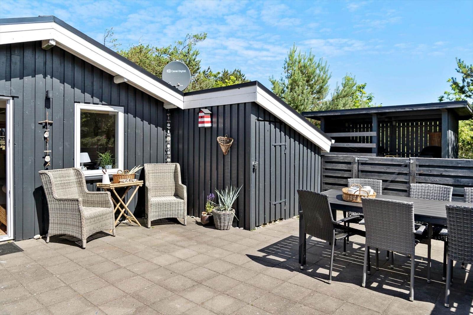 Terrasse mit Sitzgelegenheiten und Gartenbereich vor einem dunkelgrauen Haus.