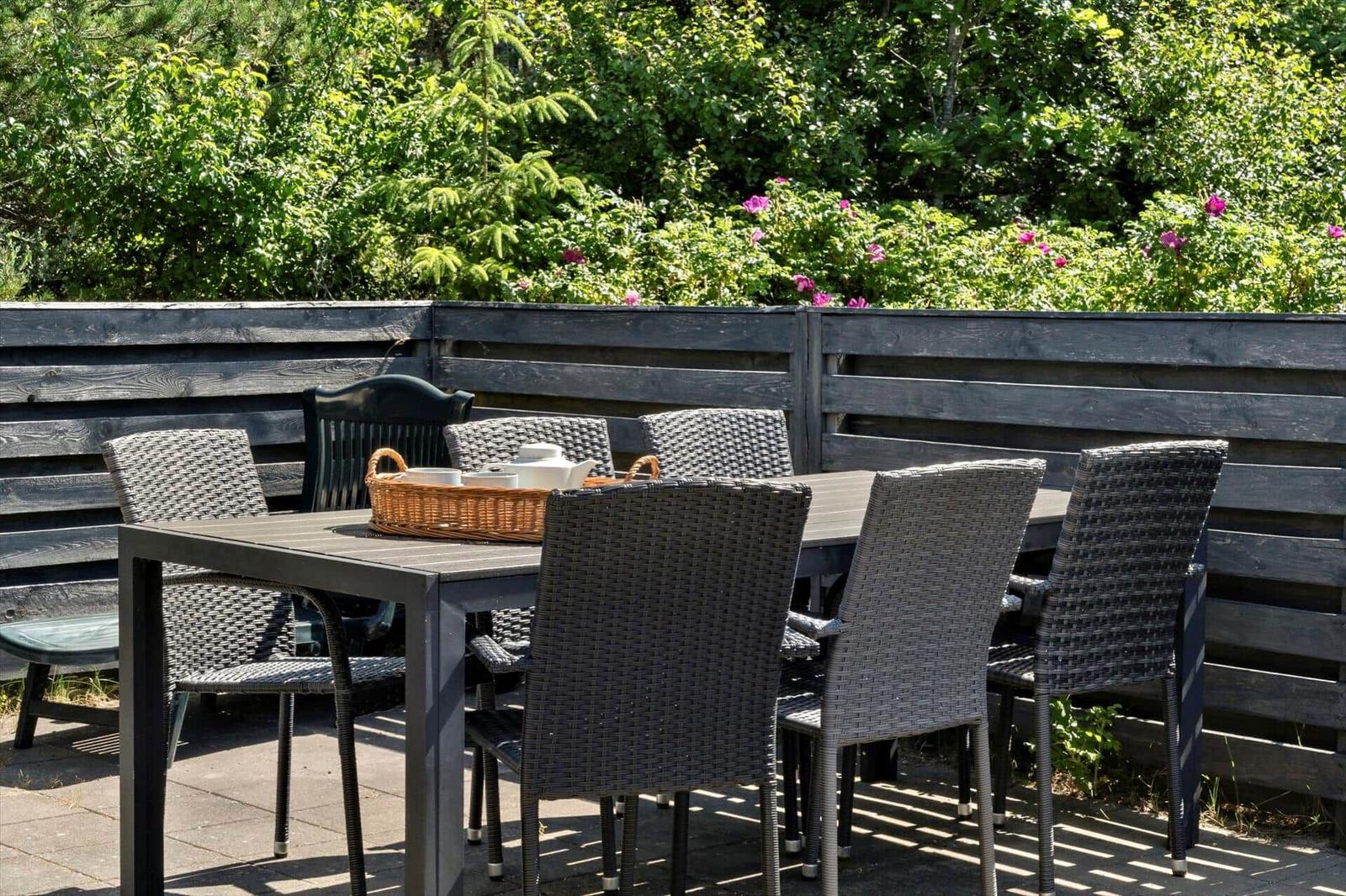 Terrasse mit Tisch und Stühlen, umgeben von grüner Vegetation und einem Holzzaun.