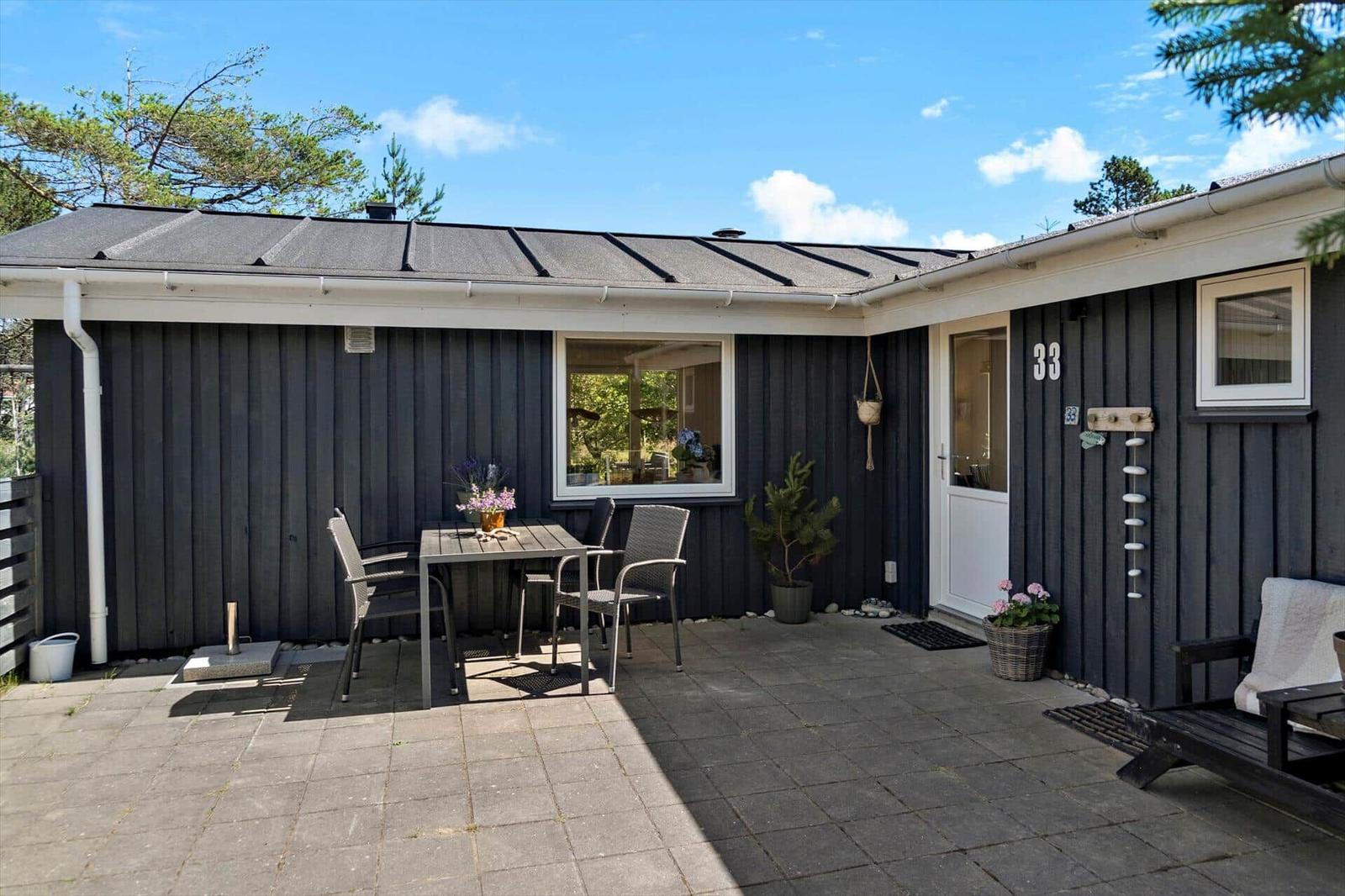Haus mit Terrasse, Tisch, Stühlen und Pflanzen. Tür mit Hausnummer 33.