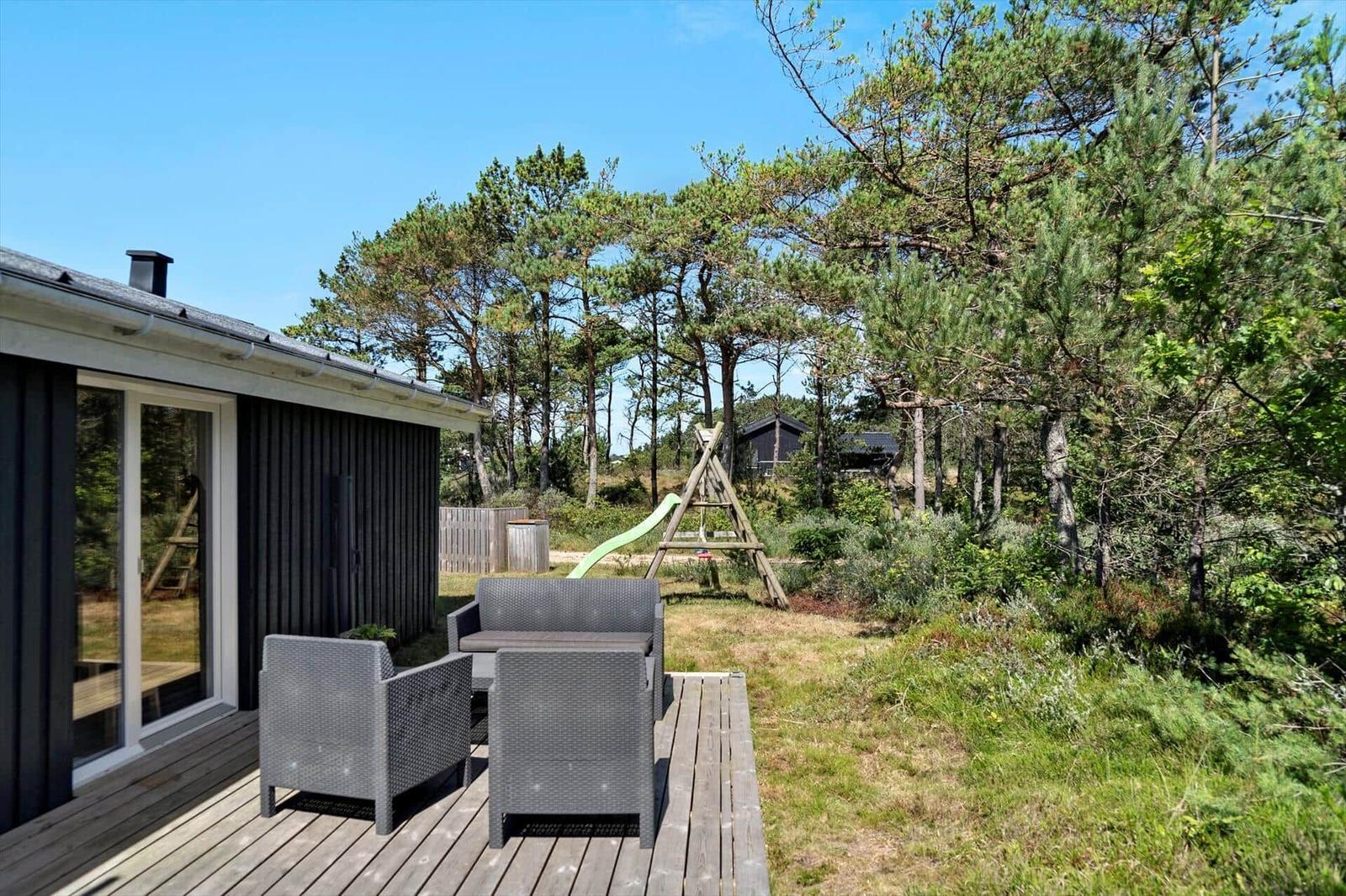 Terrasse mit Sitzgruppe, Spielplatz und Wald im Hintergrund.