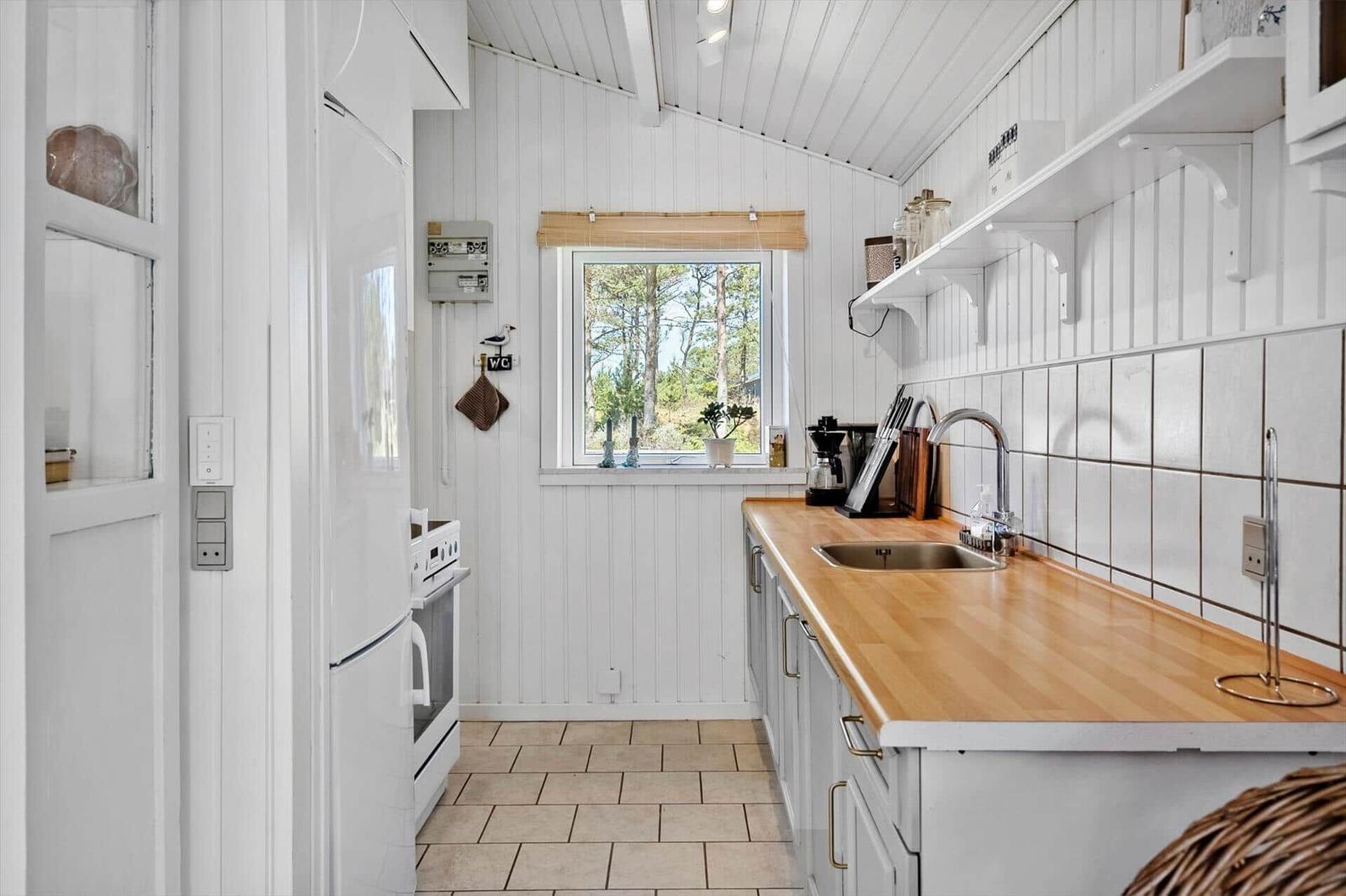 Küche mit Holzplatte, weißen Schränken und Fenster zum Wald.