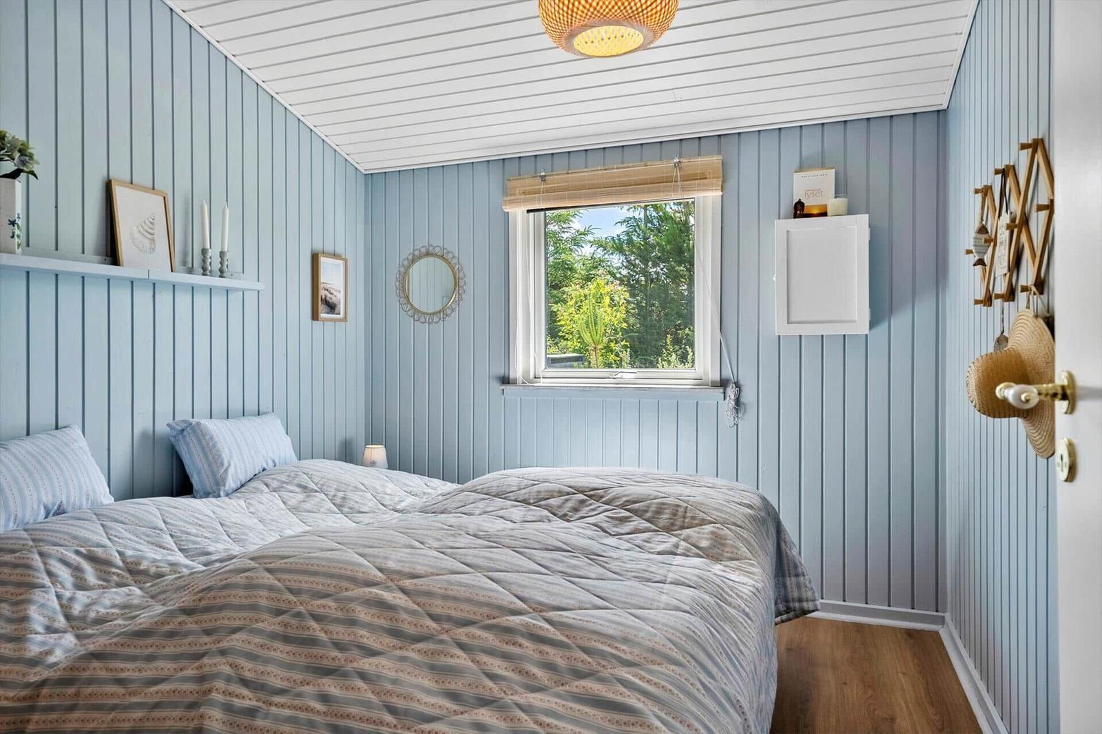 Schlafzimmer mit blauen Wänden, Bett und Fenster mit Blick auf Grün.