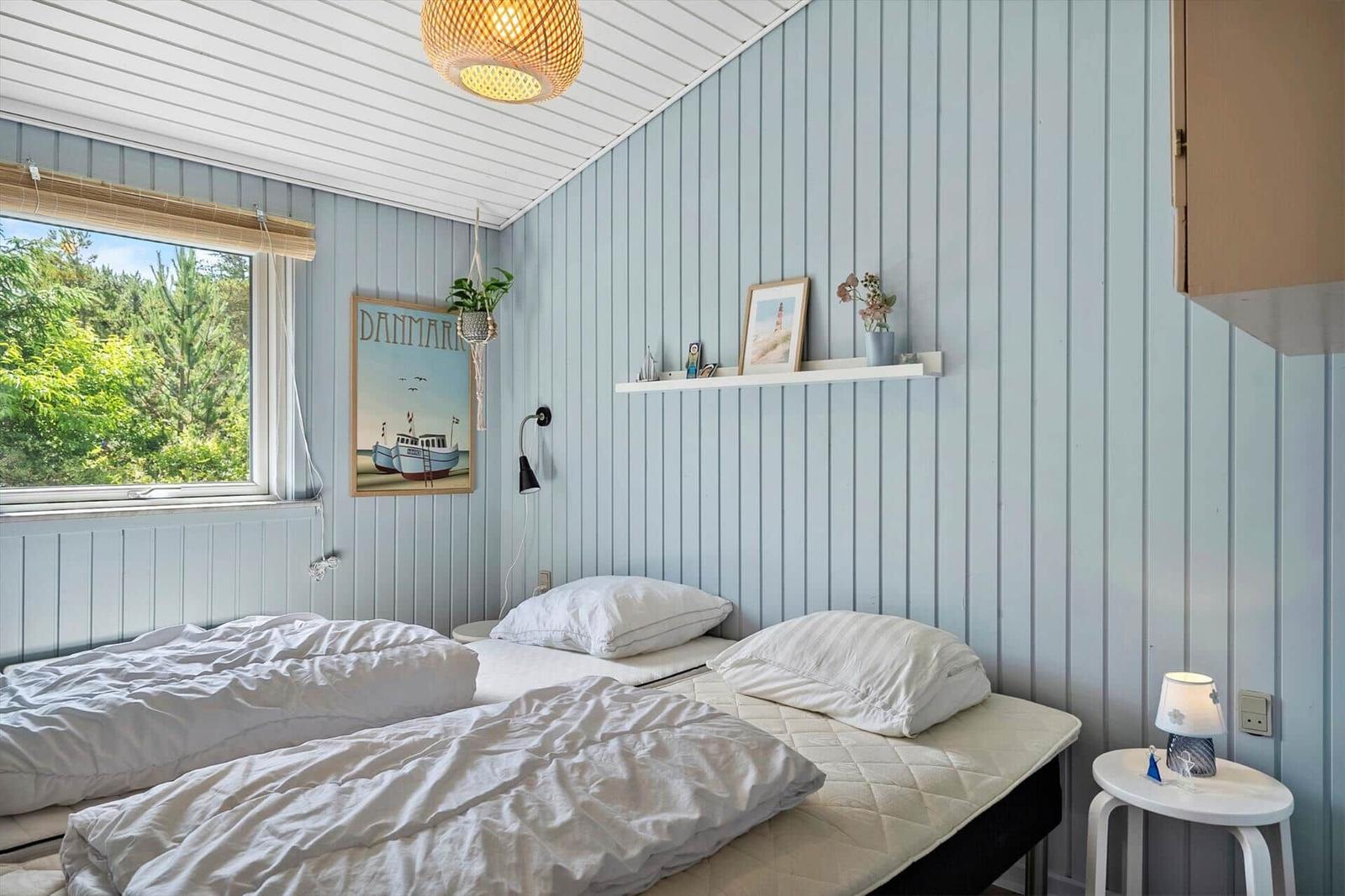 Schlafzimmer mit zwei Betten, Fensterblick auf Grün, Wandregal und Deckenleuchte.