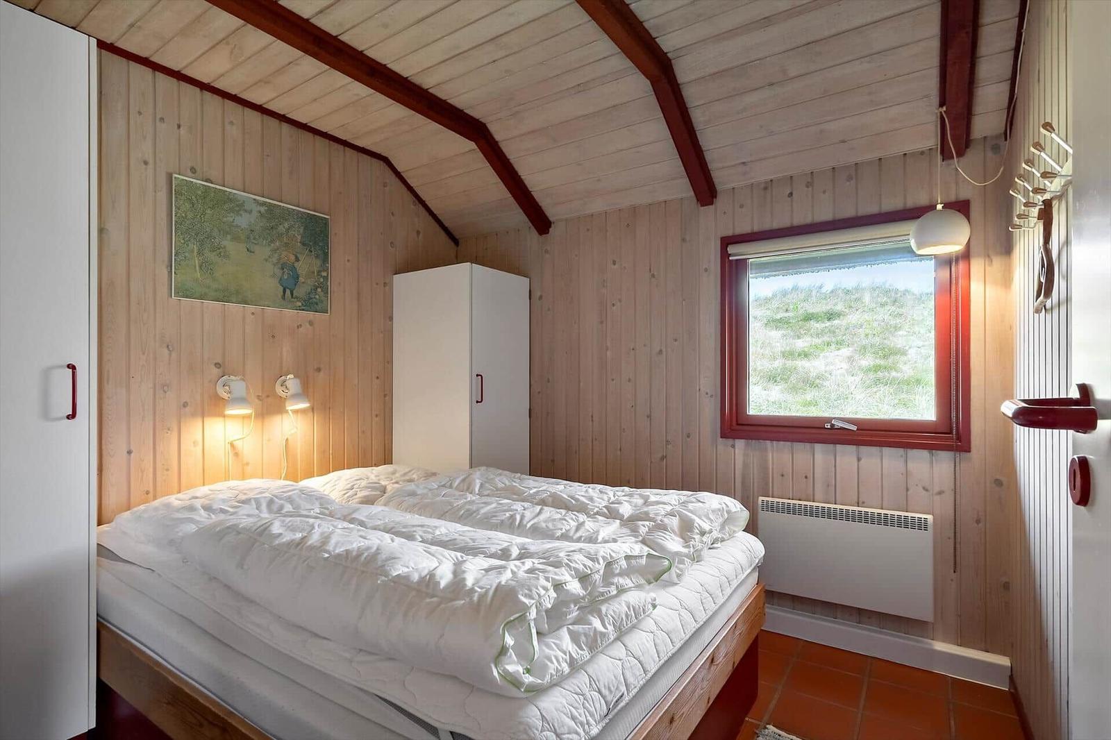 Schlafzimmer mit Holzwand, Bett, Fenster und Schrank