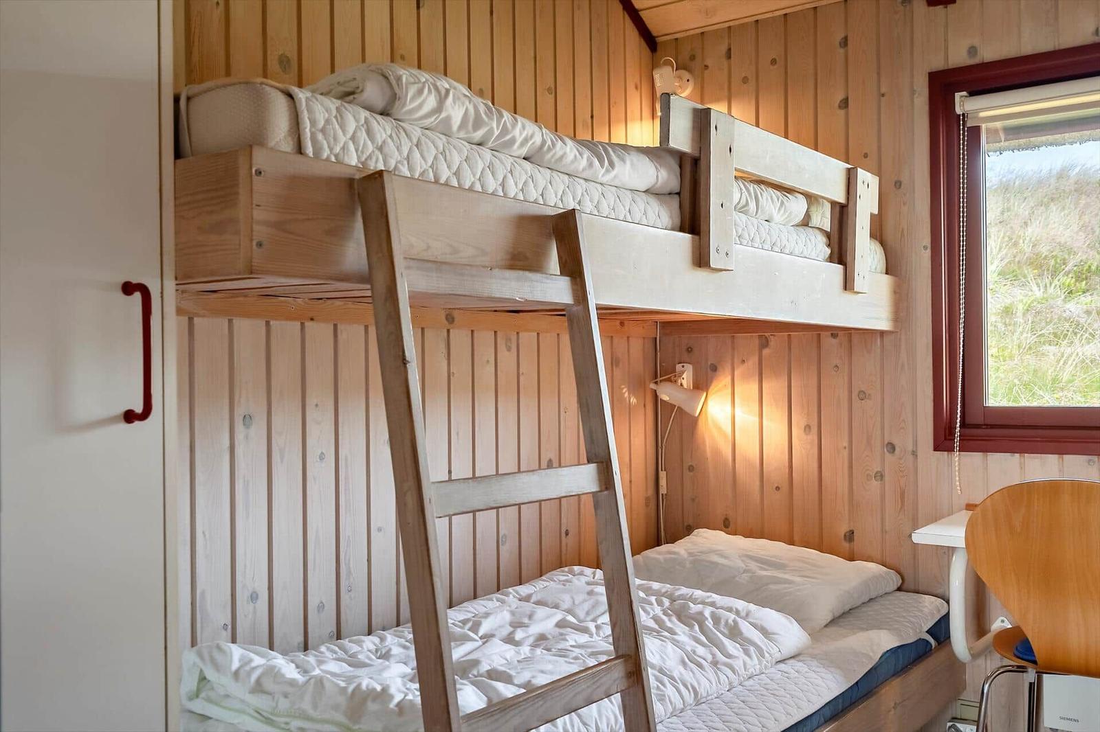 Doppelstockbett mit Matratzen und Kissen, Holzwände, Fenster und Stuhl.